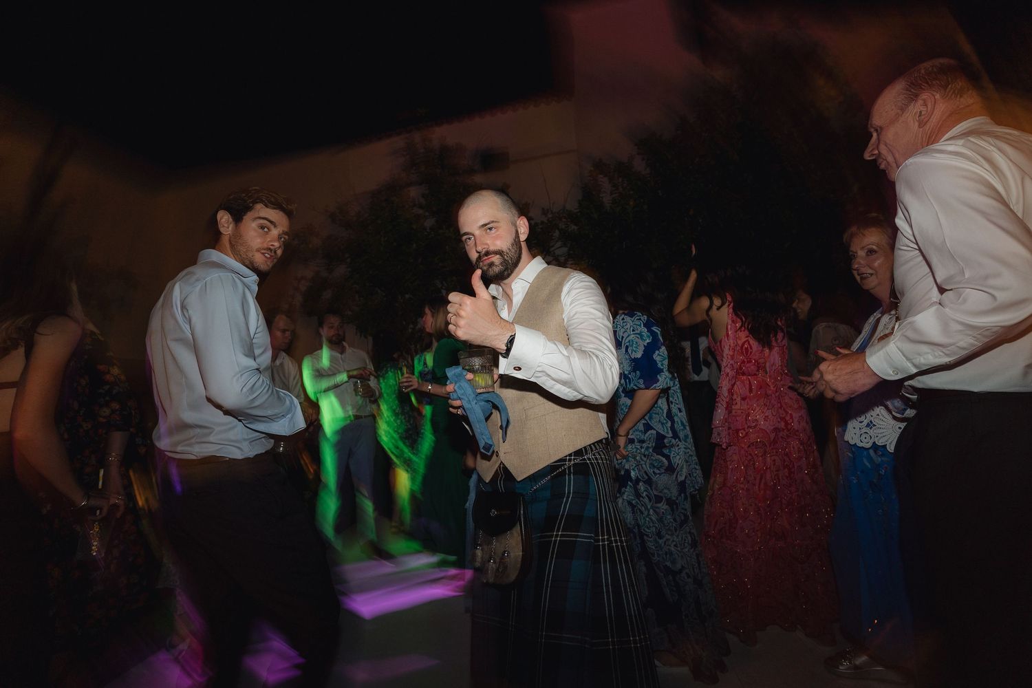 Dancers moving to music under green and purple party lights at an indoor venue.