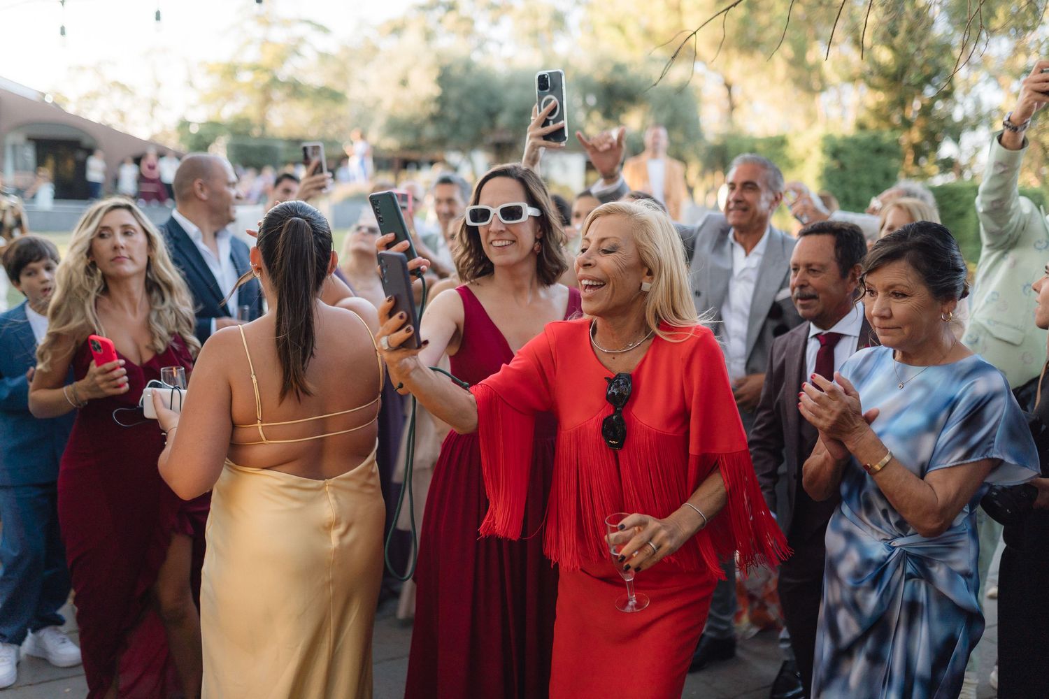 Wedding guests dancing and celebrating in colorful attire at outdoor venue.