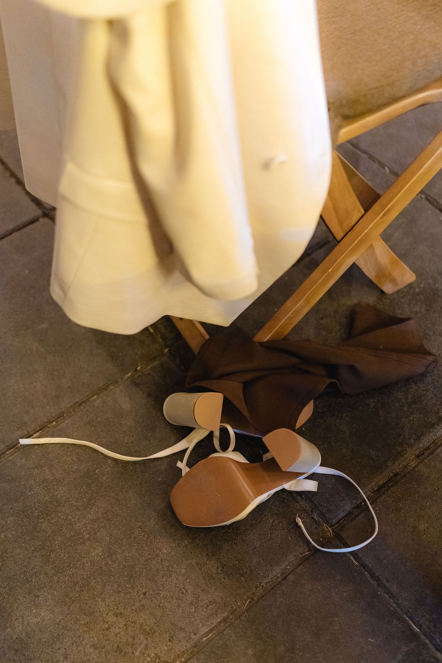 Close-up of brown sandals and white dress hem on concrete floor.