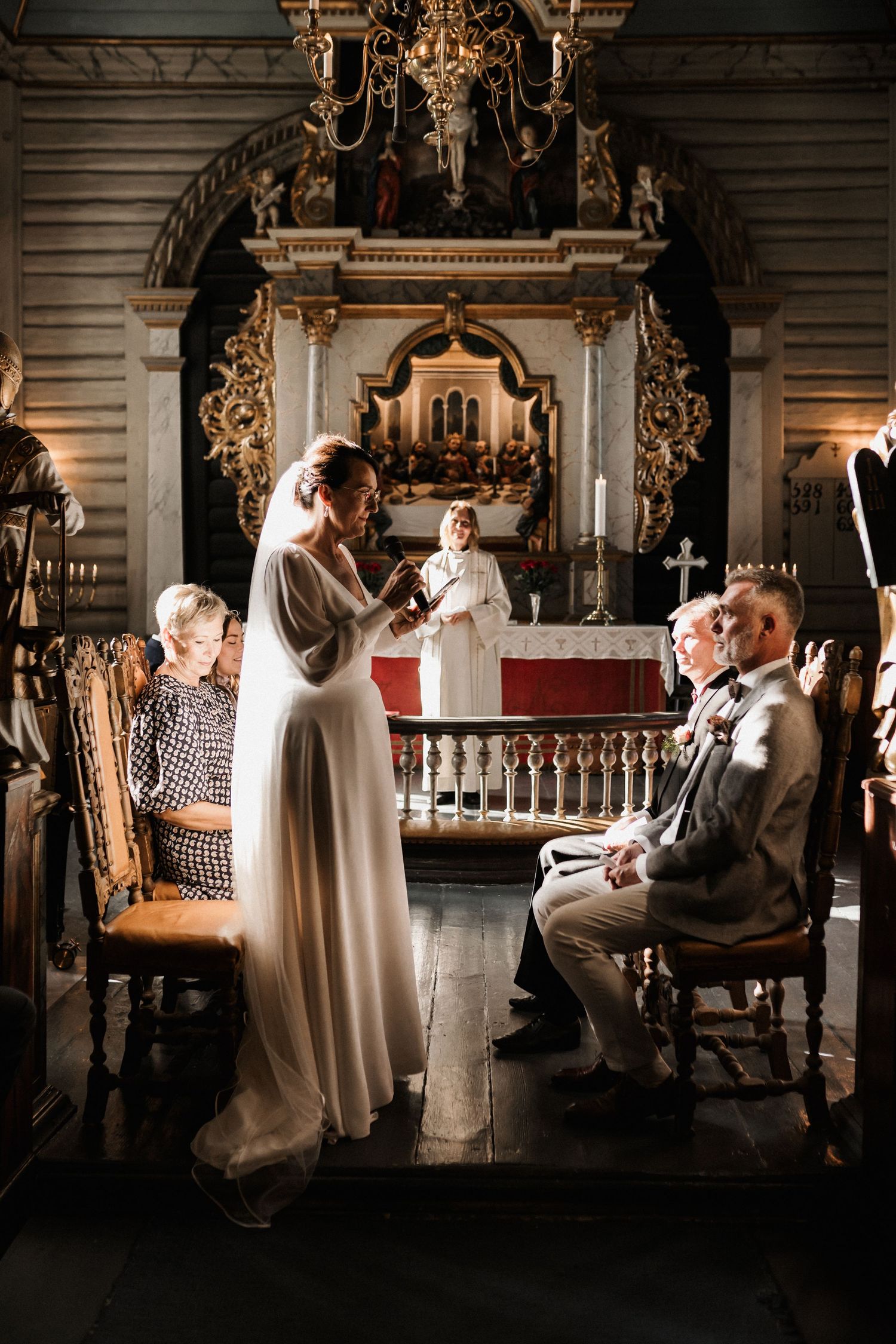 An intimate wedding ceremony takes place in a historic church with ornate baroque details and candlelight.