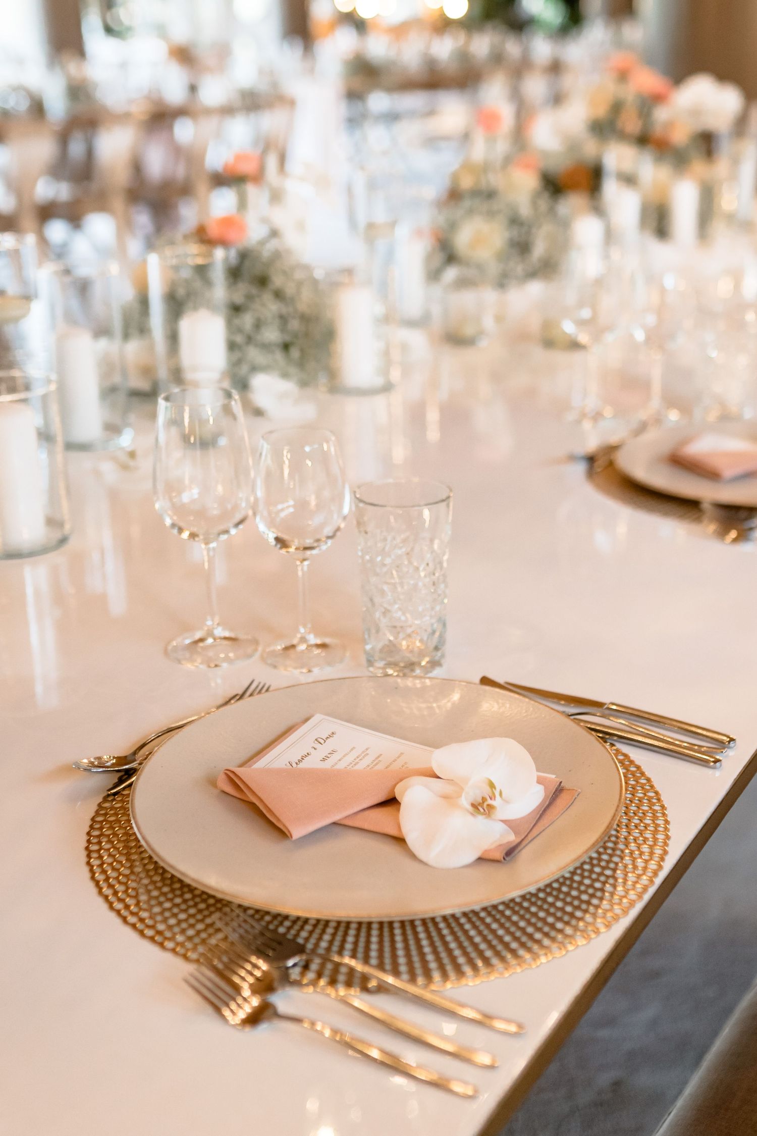 Elegant wedding table setting with gold charger plates, crystal glasses and peach napkins.