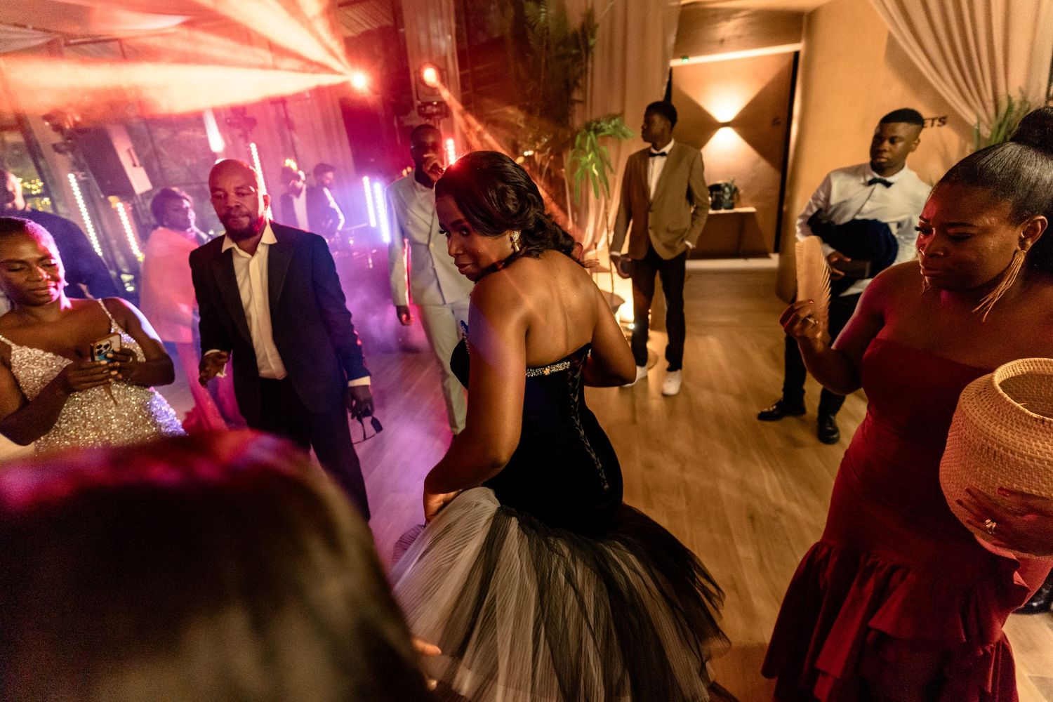 Wedding reception dance party with colorful lighting and guests in formal attire.