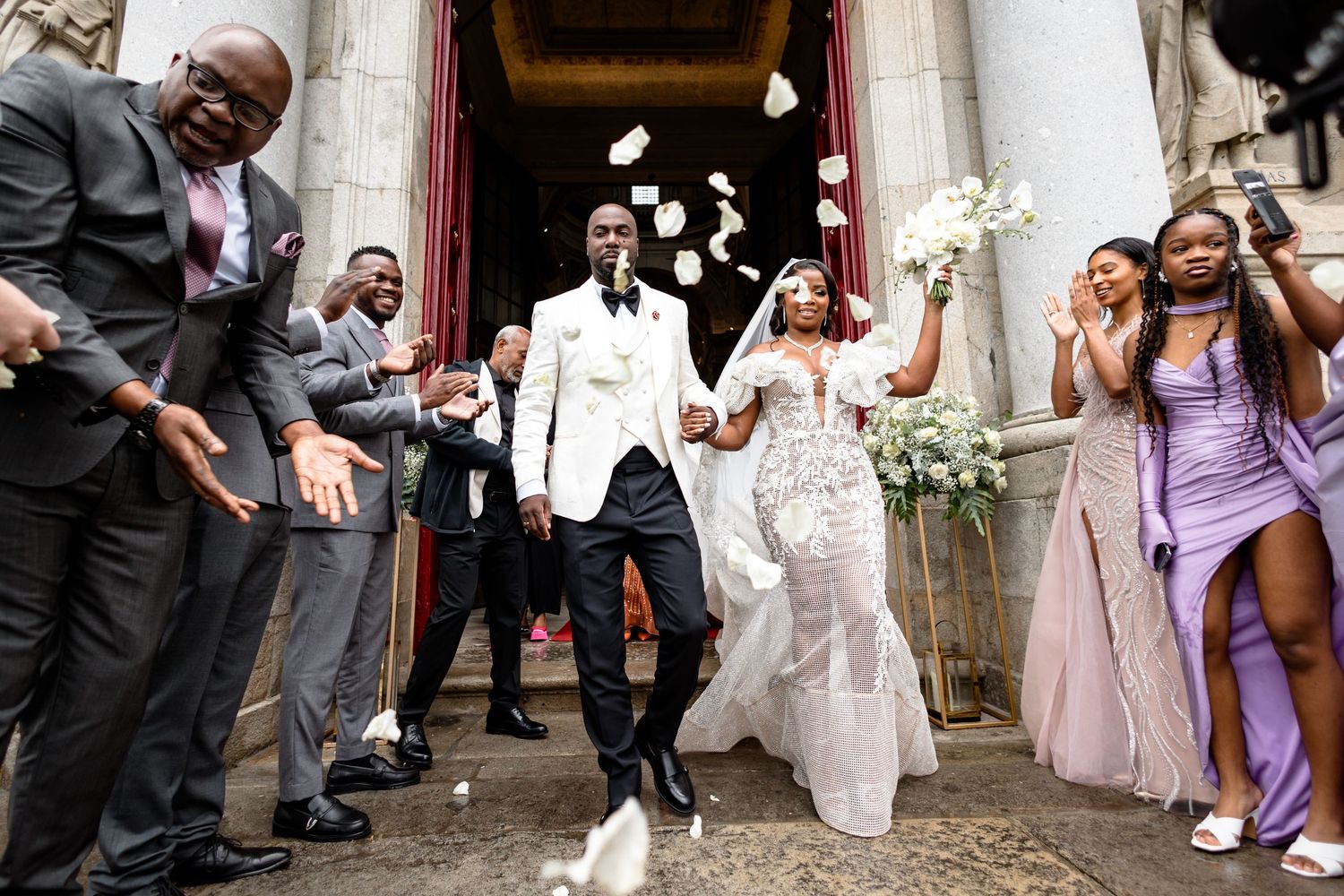 Newlyweds exit church as guests throw flower petals in celebration.