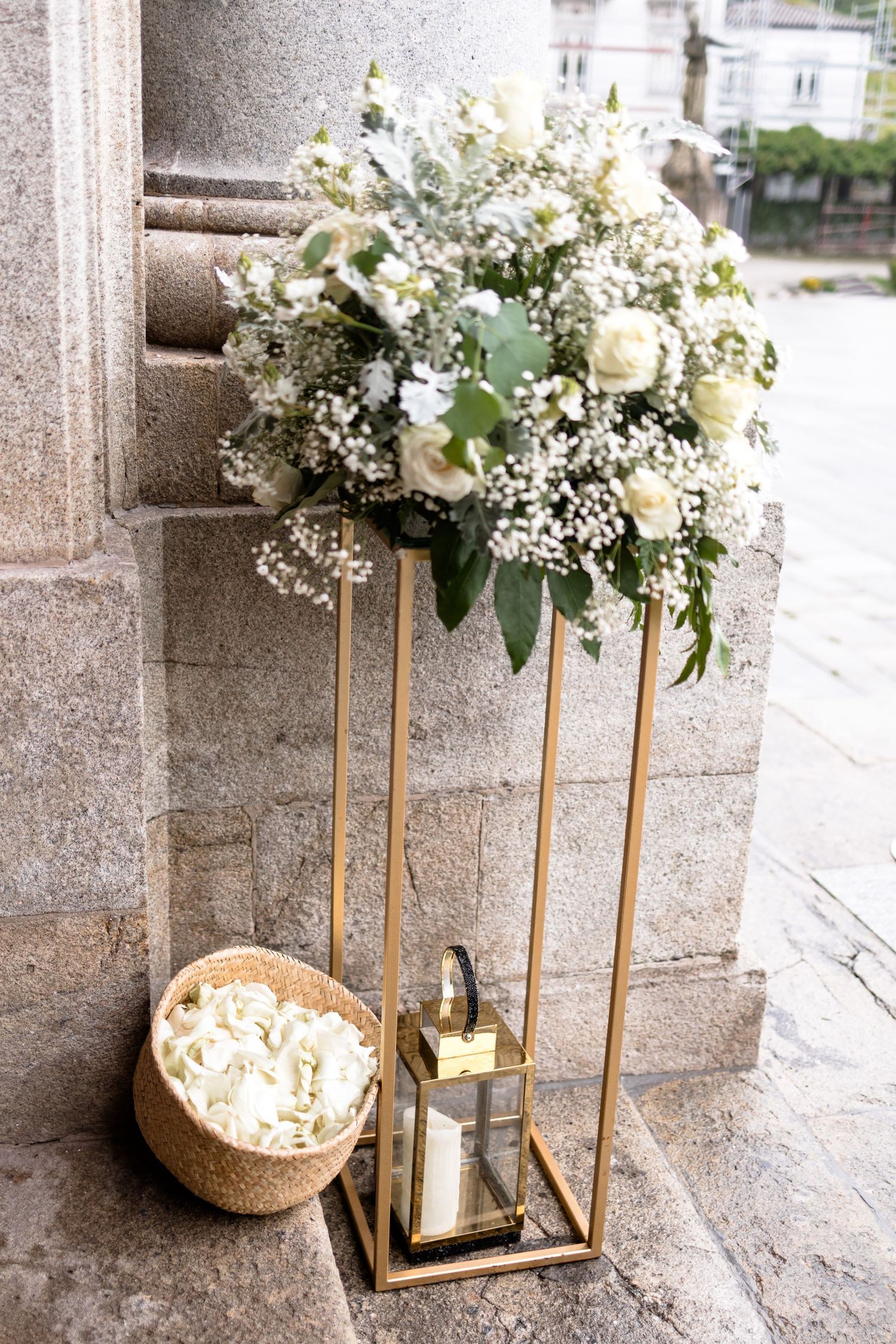 Elegant white floral arrangements in gold lanterns displayed against a stone wall.