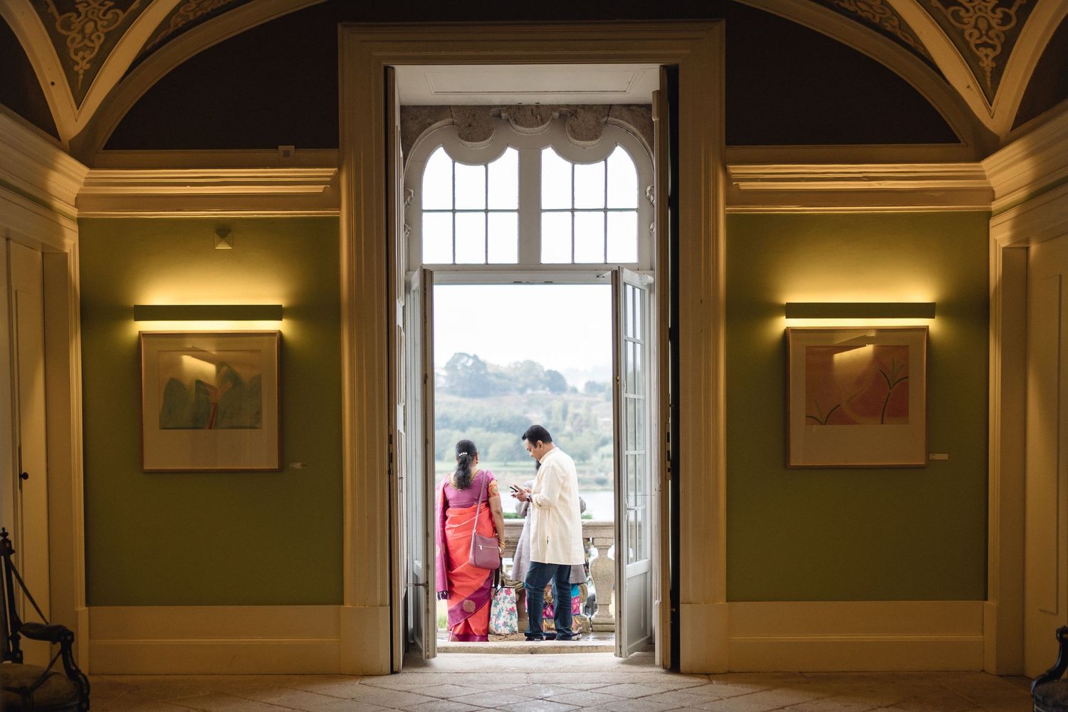 Two people in traditional dress stand silhouetted in an ornate doorway with green walls and golden architectural details.