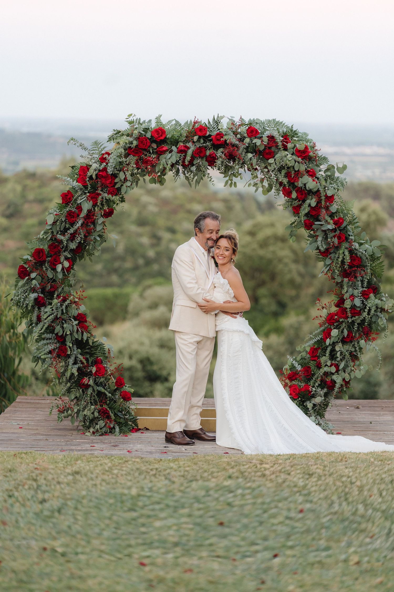 Beautiful wedding scene with red floral arch overlooking scenic landscape.