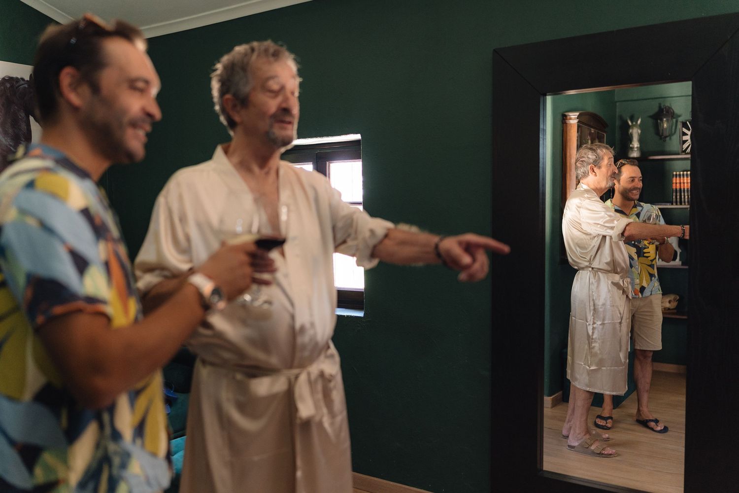 People sharing drinks and laughing while looking at their reflection in a wall mirror.