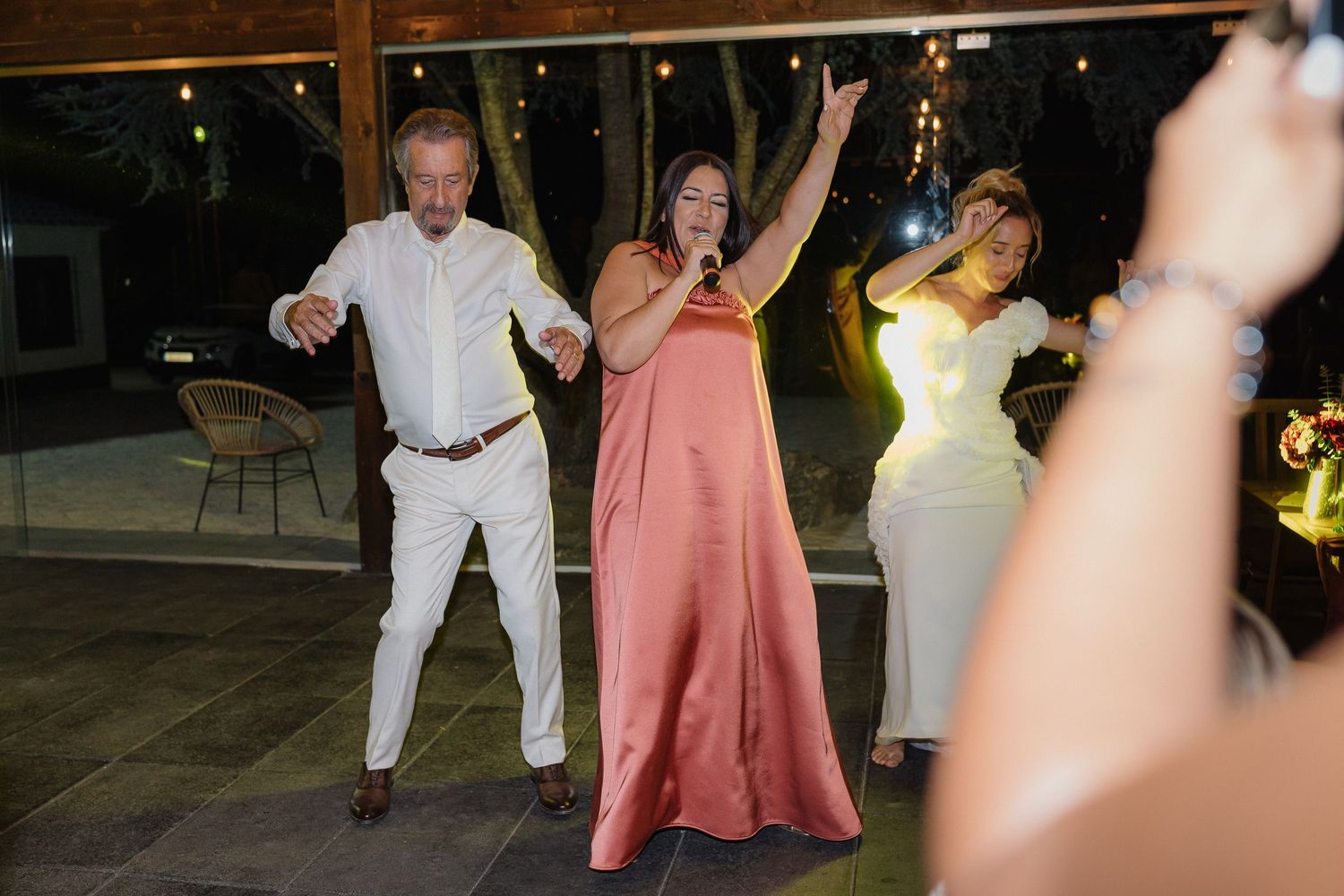 Wedding guests dance and celebrate on an outdoor patio decorated with string lights at night.