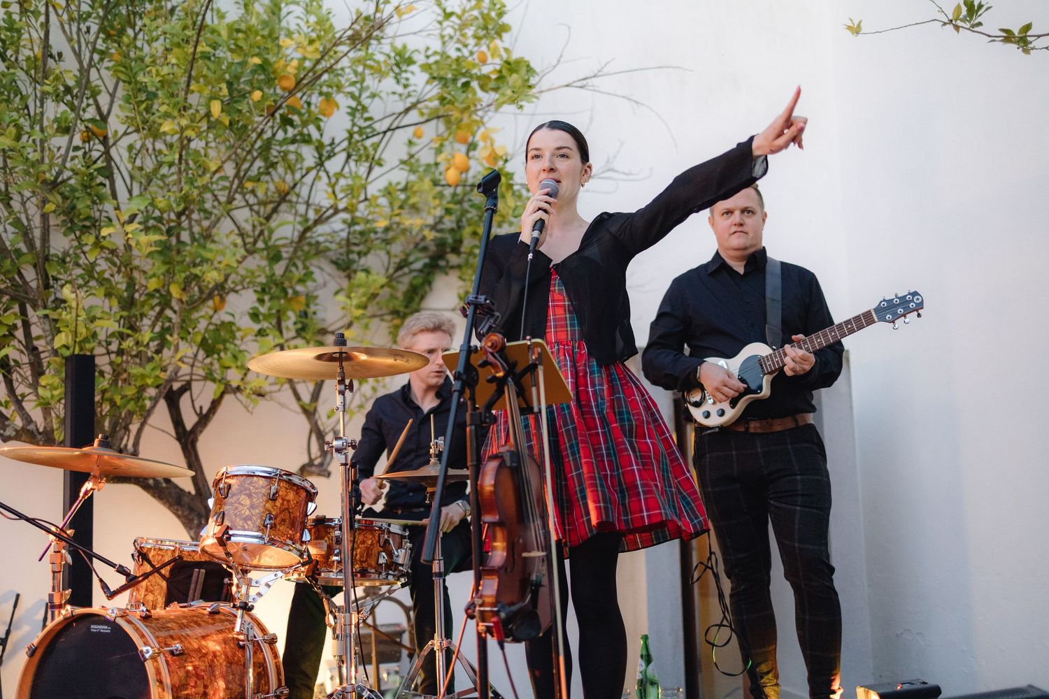 Musicians perform energetically on stage with instruments at outdoor venue.