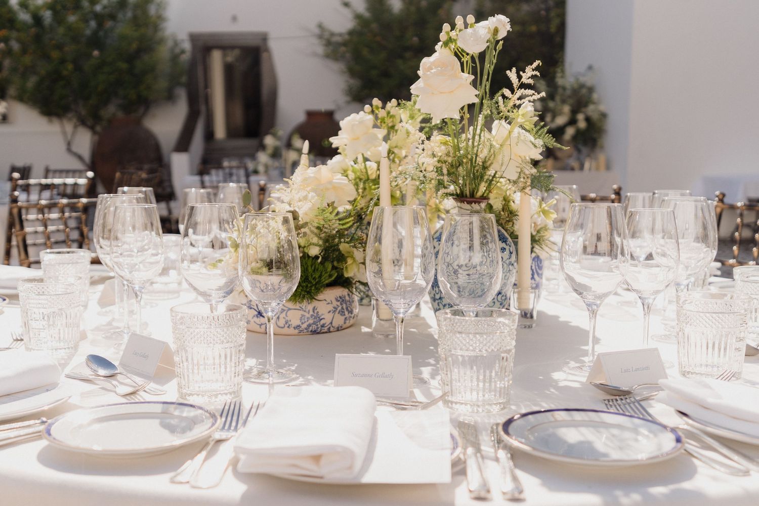 White and cream floral centerpieces with delicate glassware on tables set for a formal dining event.