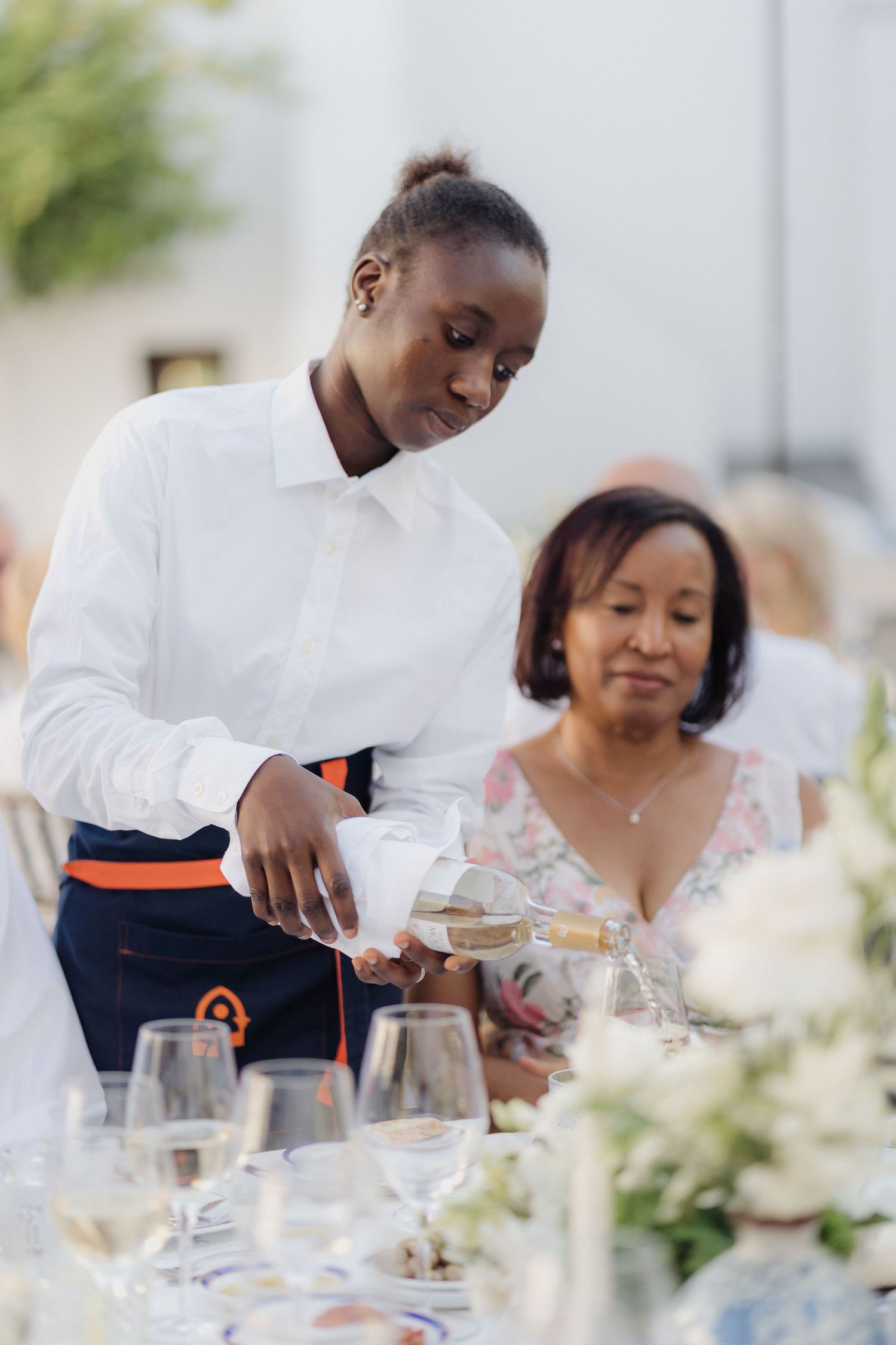 Guests being served at an elegant outdoor dinner with white floral centerpieces.