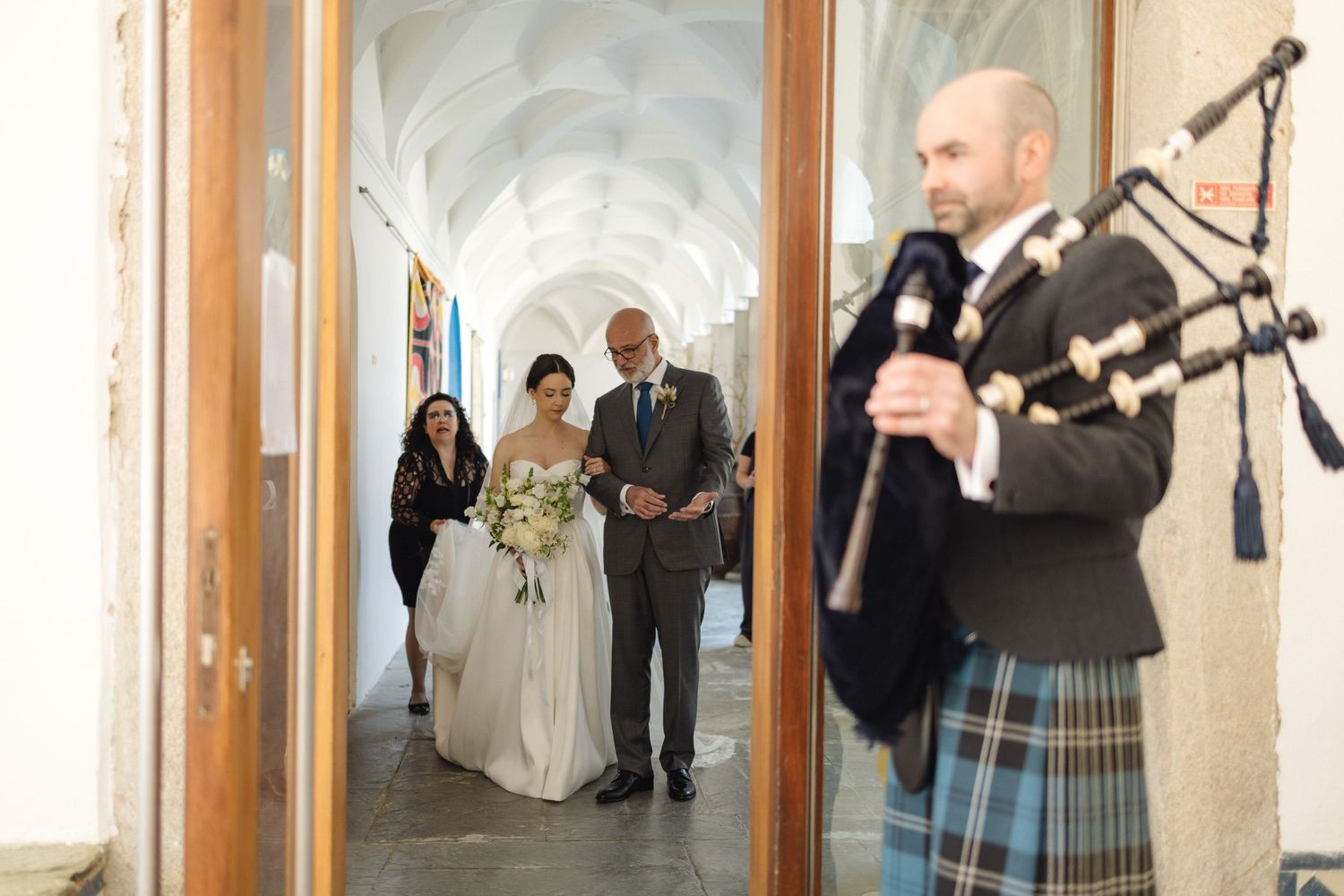 Wedding party walking through hallway with bagpiper in Scottish attire.
