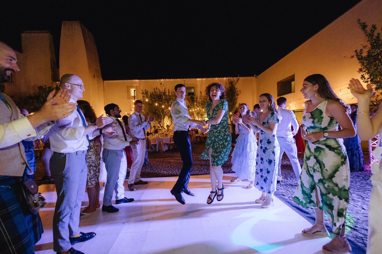 Couples dancing together on a colorfully lit reception dance floor.