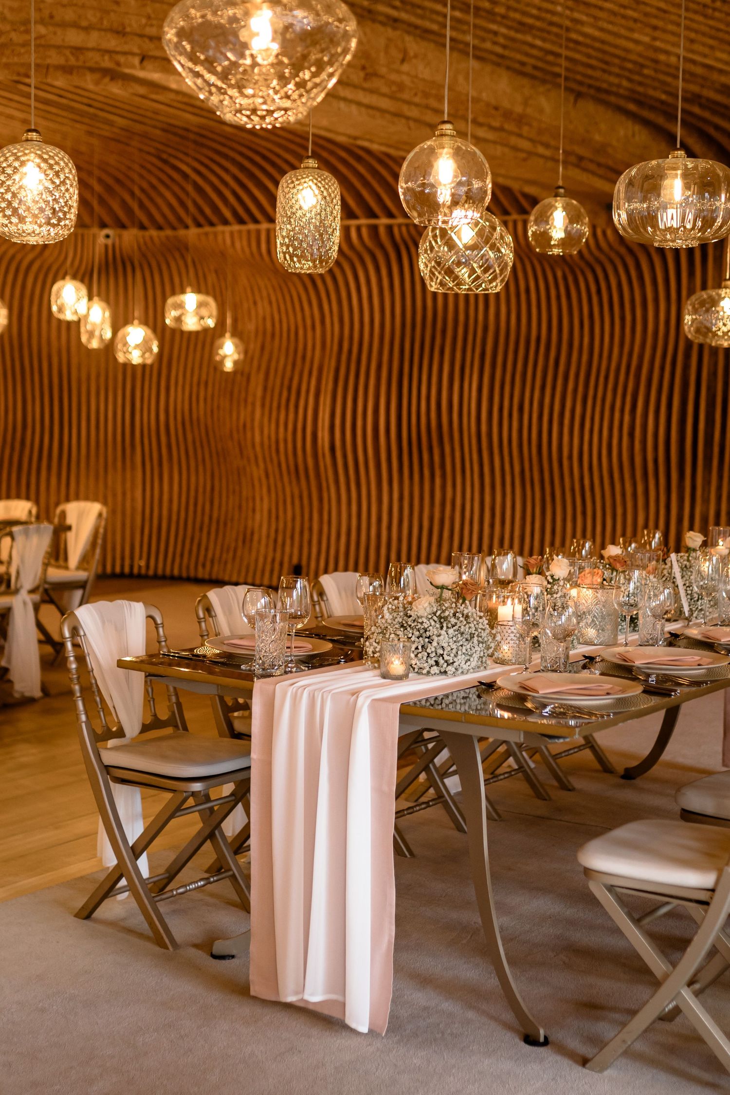 Elegant wedding reception table setup with crystal pendant lights and curved wooden ceiling.
