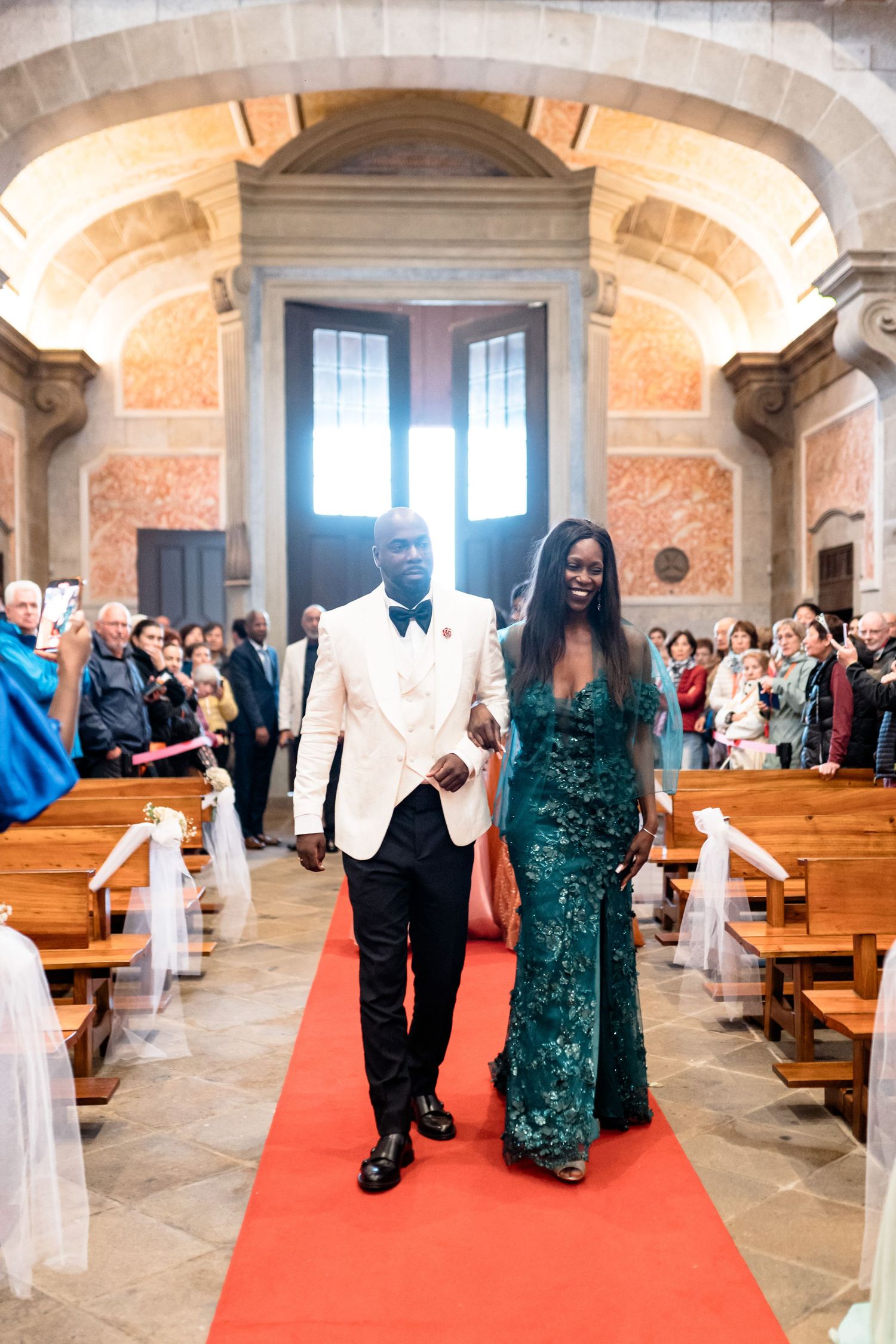 Wedding ceremony procession inside a historic church with guests walking down a red carpeted aisle.