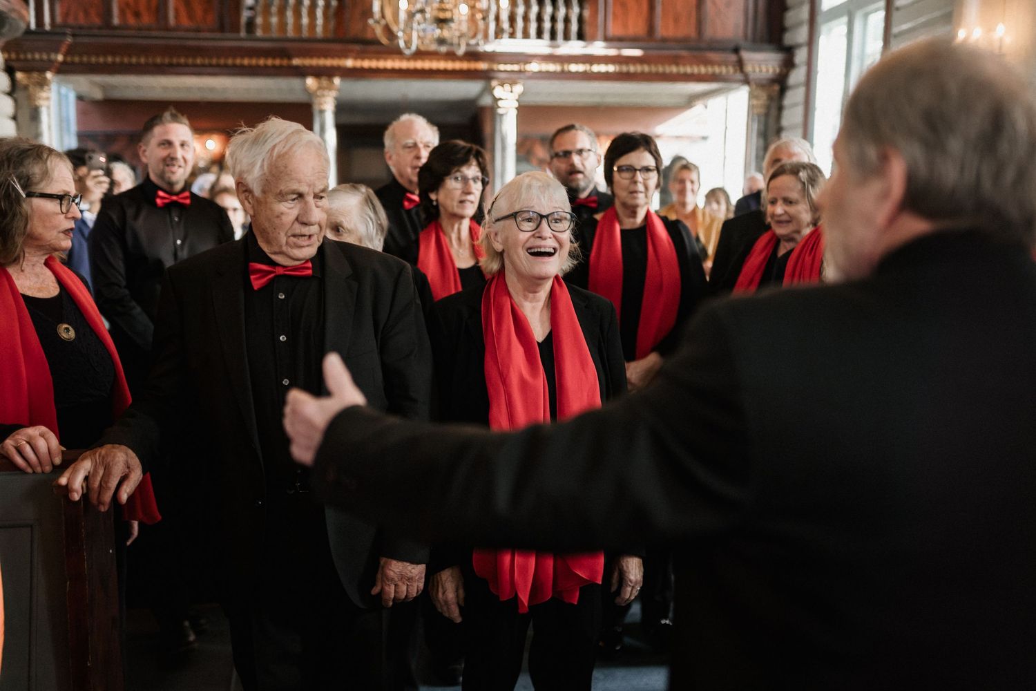 A large group wearing red scarves stands together in a dimly lit church setting.