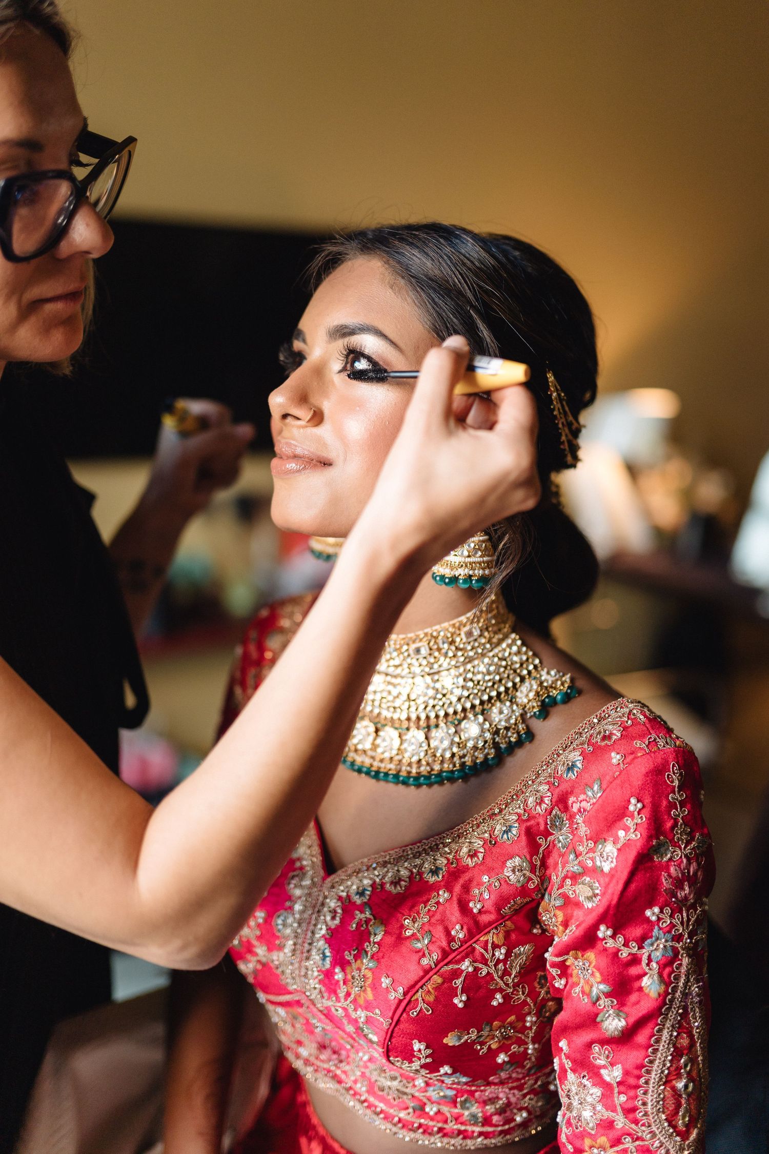 Traditional Indian bridal preparation showing detailed embroidered red lehenga and gold jewelry.
