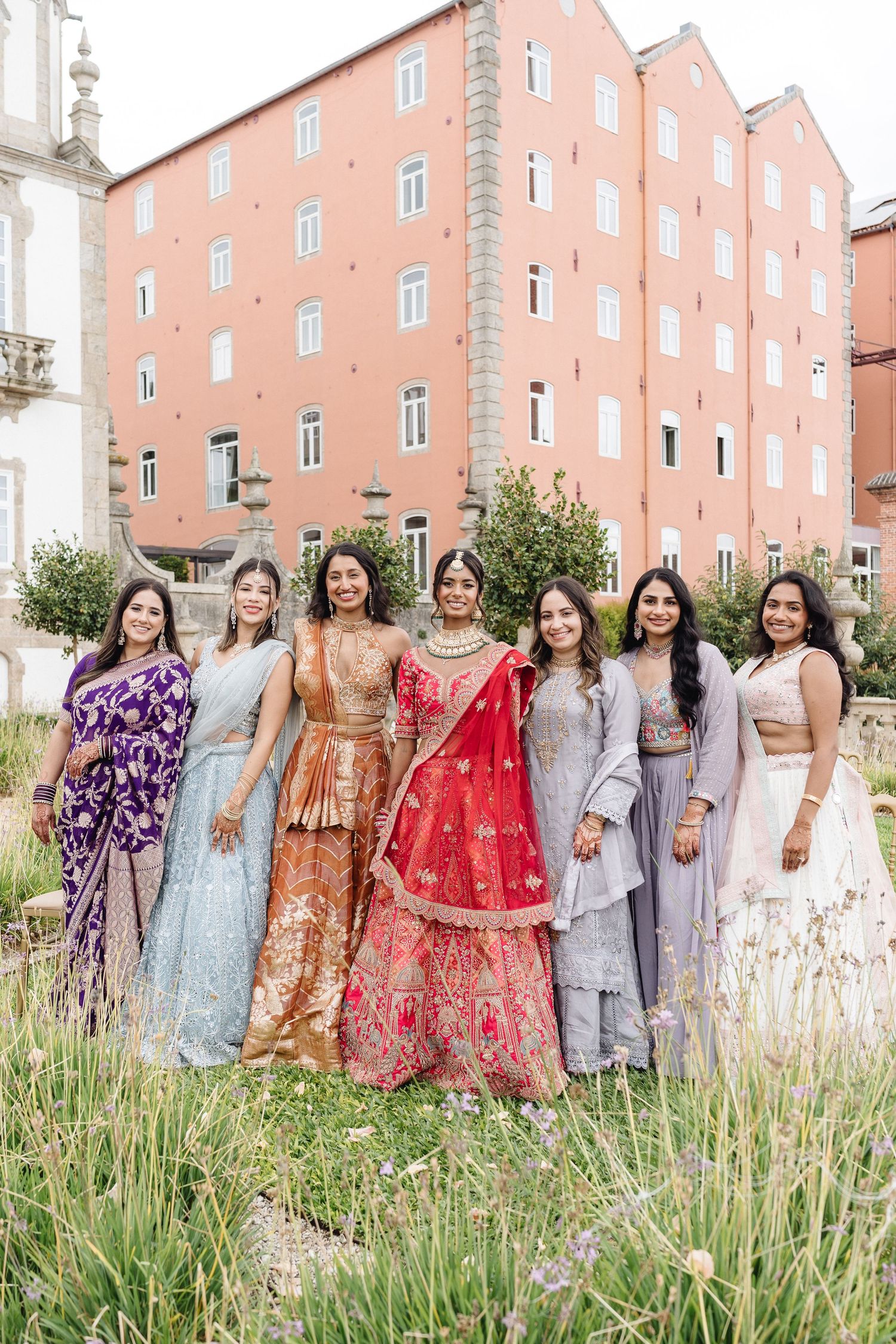 Wedding party in colorful traditional Indian dresses posing together in a garden setting.