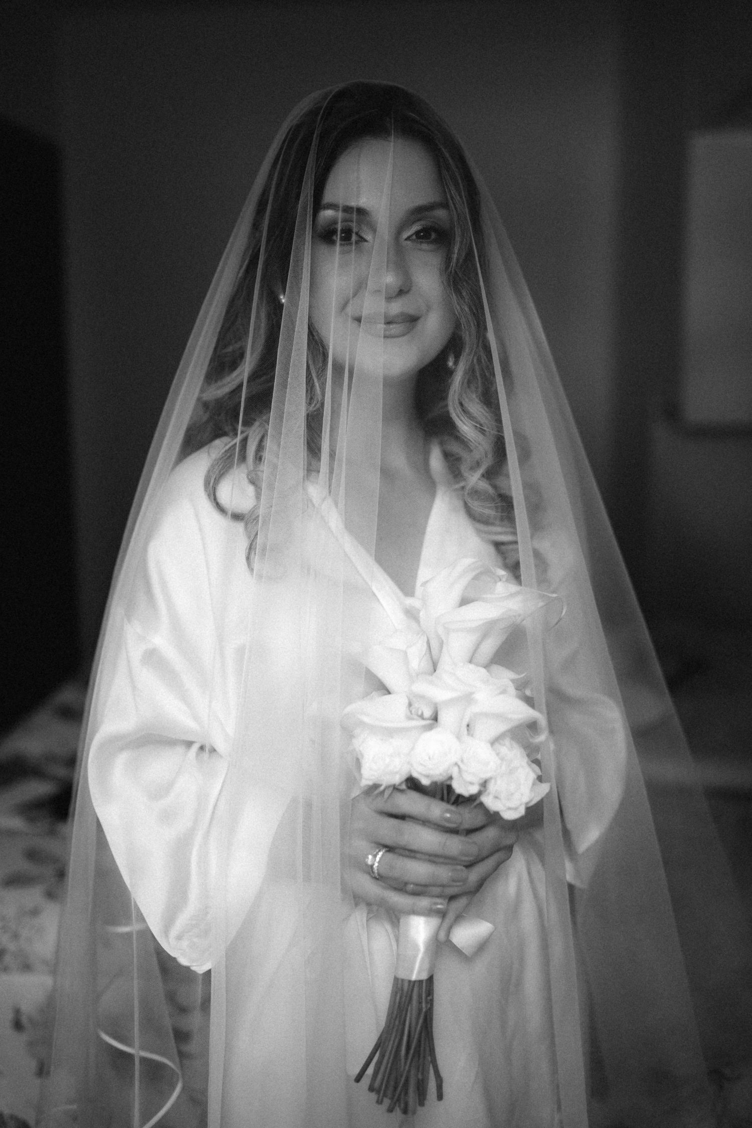 Ethereal bridal portrait showing flowing white veil and wedding bouquet in dramatic black and white.