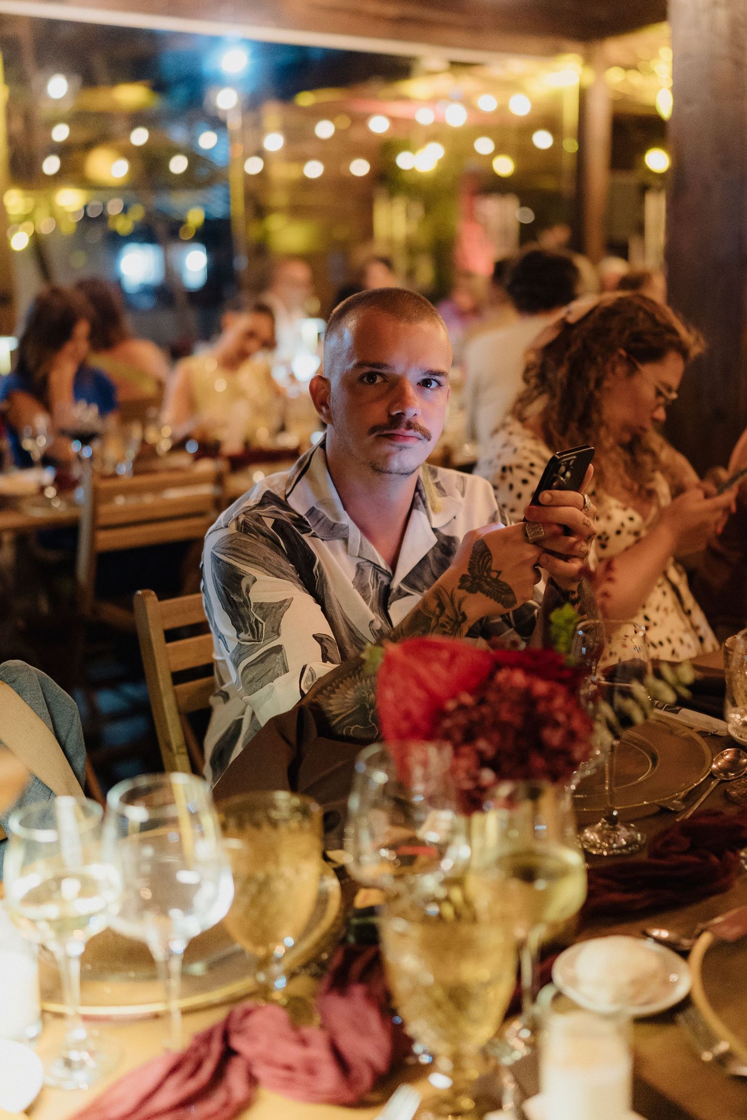 Wedding guests enjoying an elegant dinner reception with string lights and wine glasses on decorated tables.