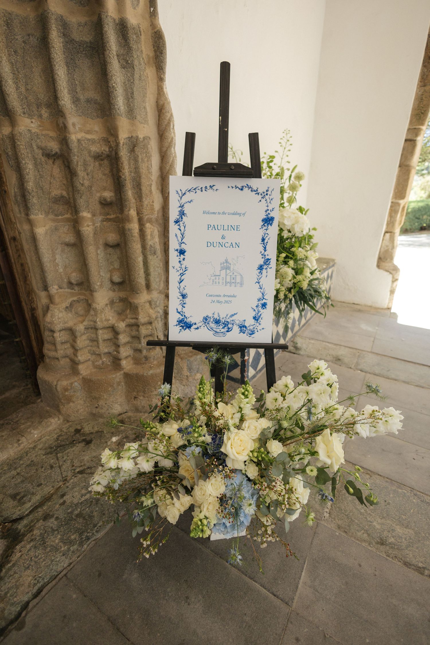 Wedding welcome sign on easel with blue floral design and white flower arrangement.