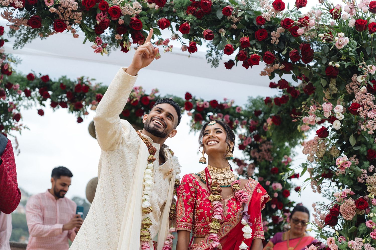 A festive outdoor wedding ceremony decorated with vibrant red roses and floral arrangements.