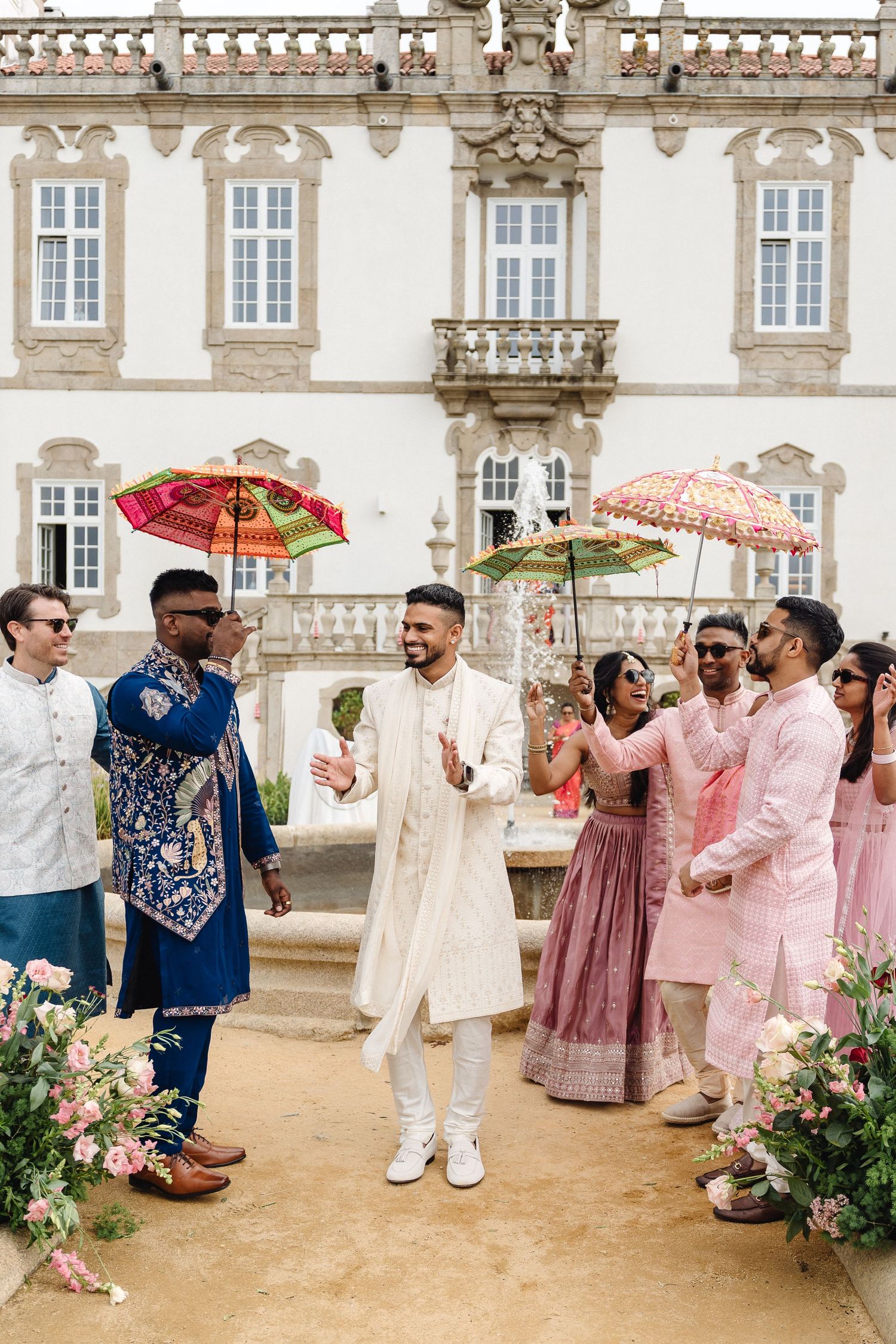 Wedding party in traditional Indian attire dancing with decorative umbrellas at an outdoor venue.