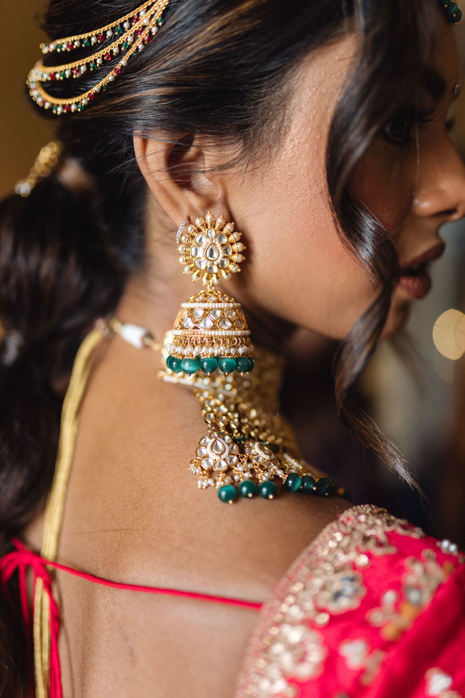 Ornate gold and emerald jhumka earring with pearl details shown in profile against a blurred background.