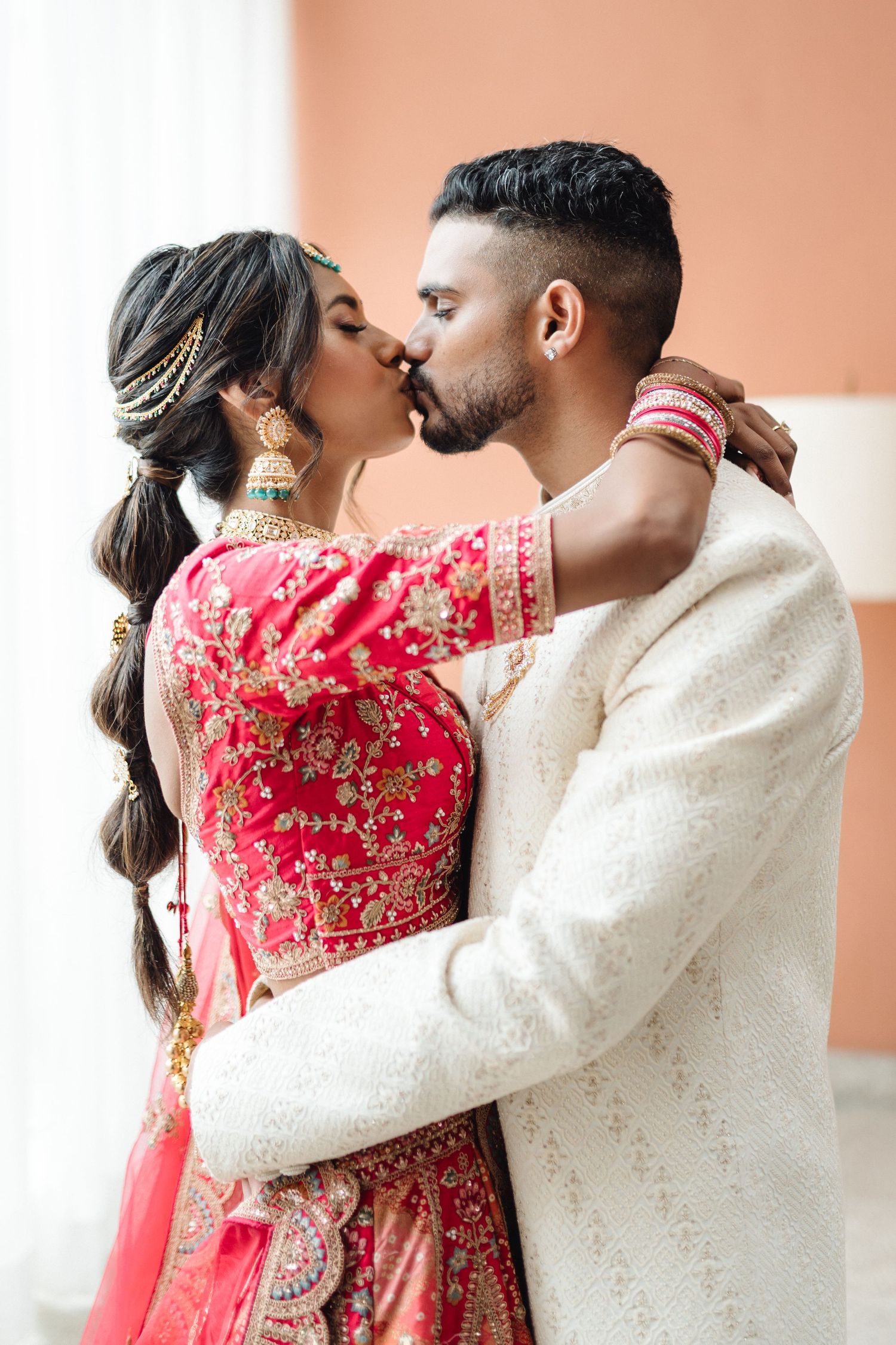 Romantic moment captured in traditional Indian wedding attire with red and cream colors.