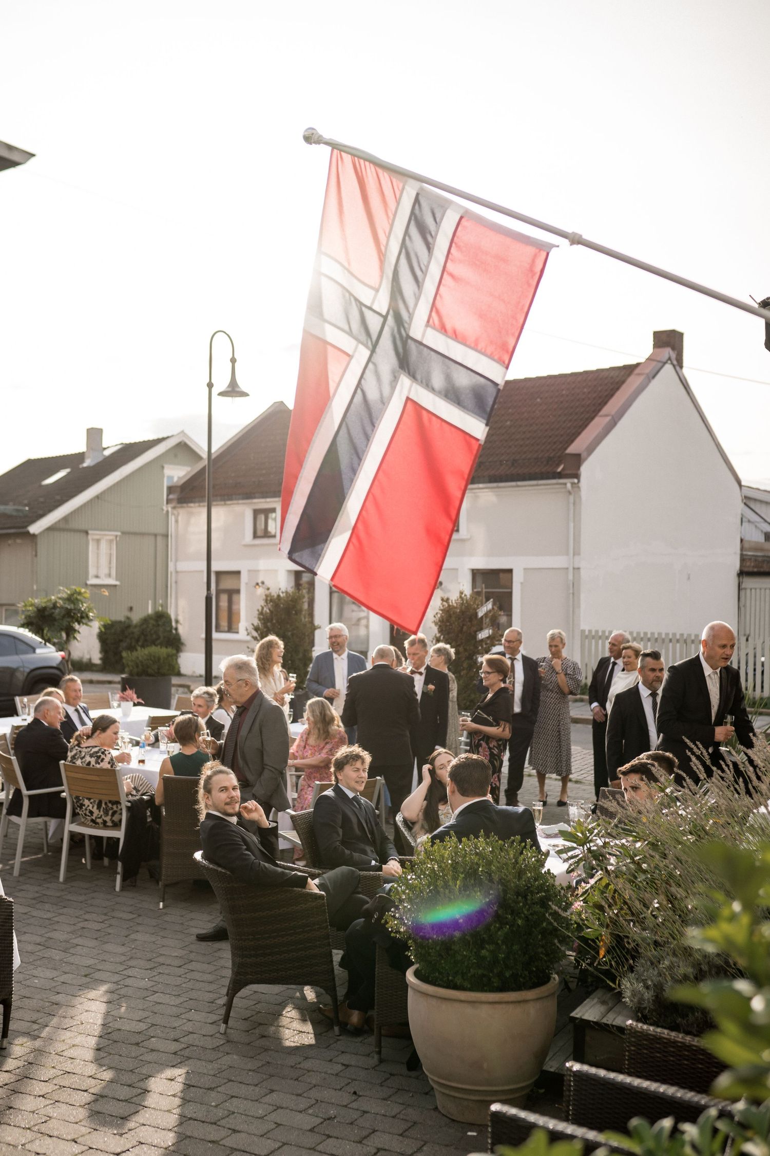 Outdoor dining event with red banners and guests seated at tables on a patio near white buildings.