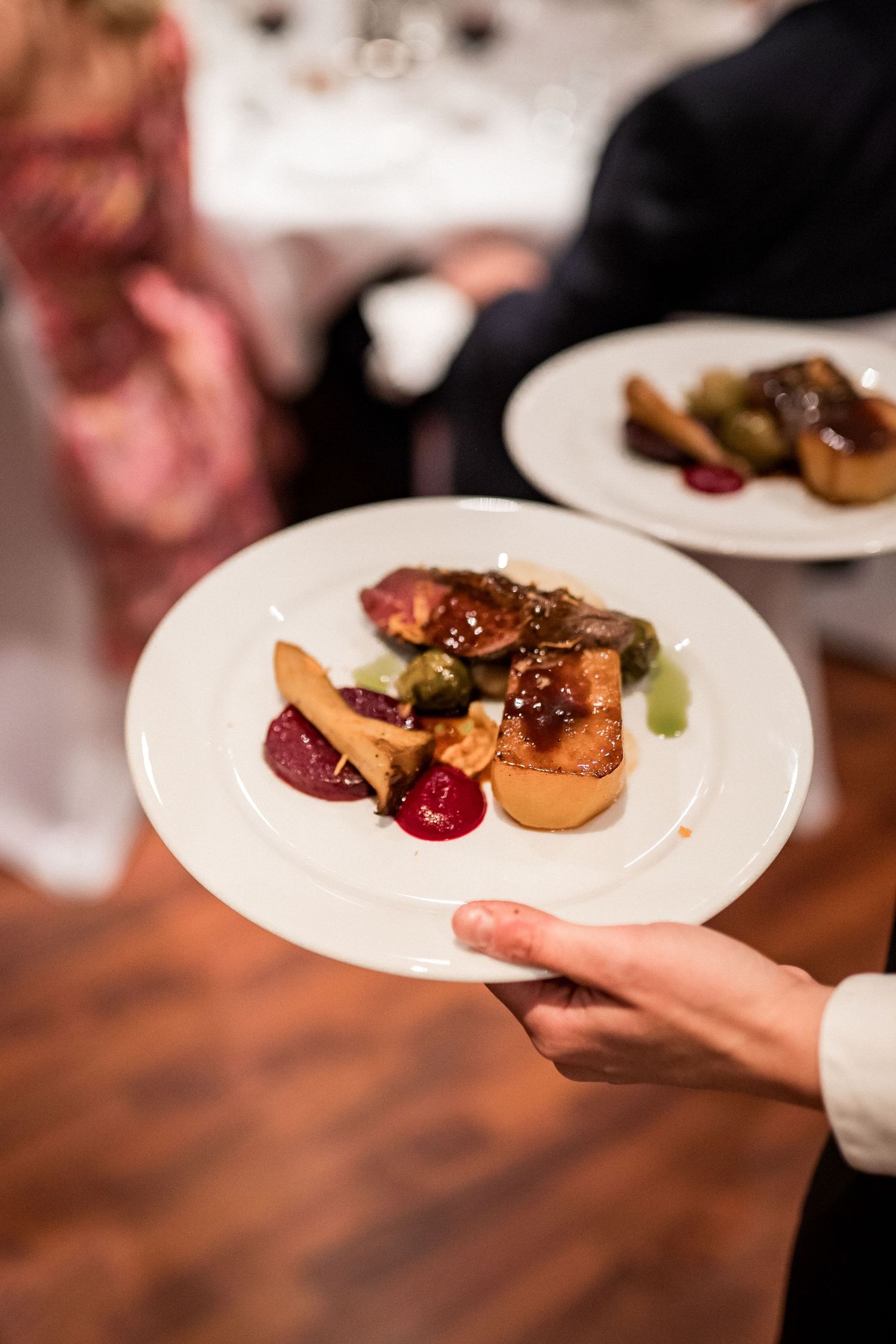 Plates of glazed meat dishes being served at an upscale dining event.