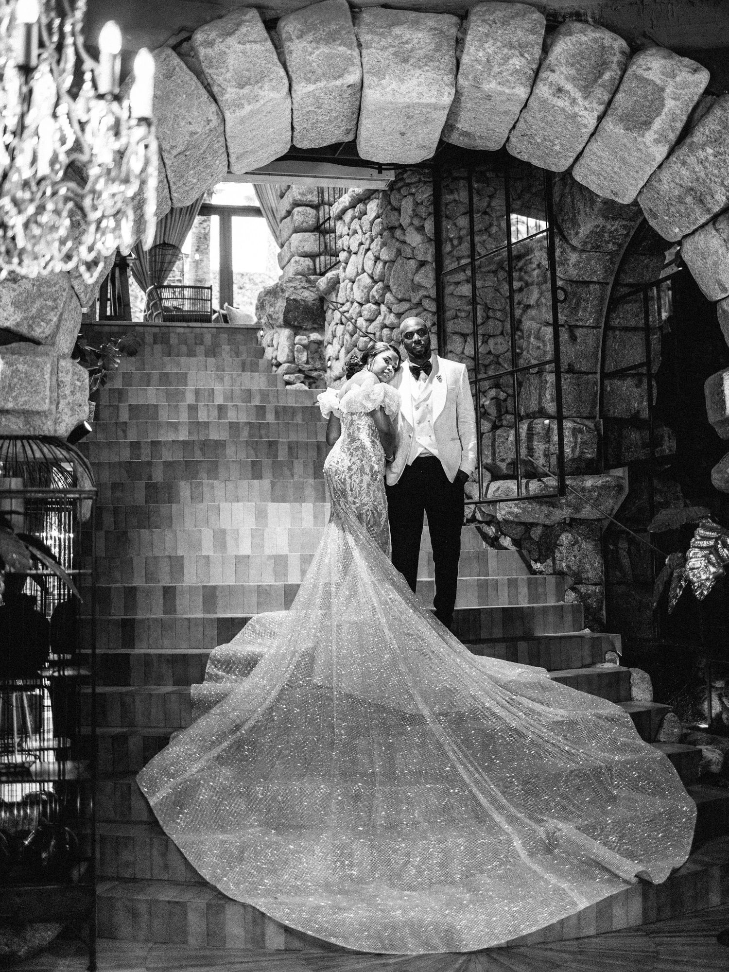 A dramatic black and white wedding photo under a stone archway with a flowing cathedral veil.