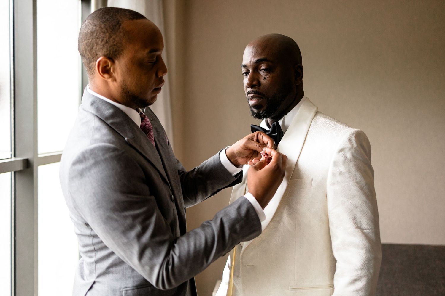Two men in formal suits helping with wedding preparations.