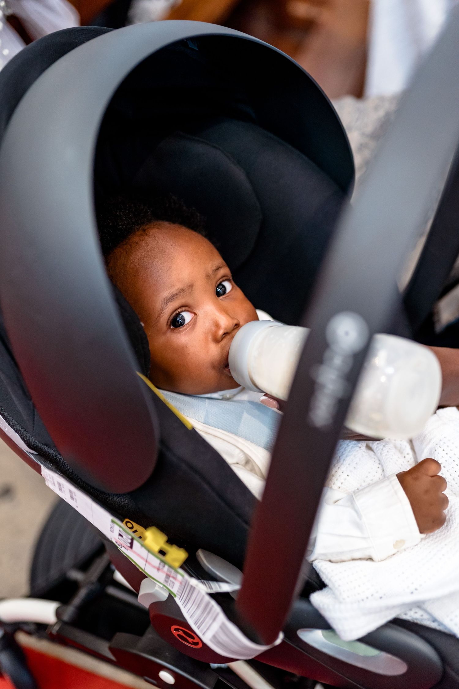 A child in a car seat wearing a white outfit.