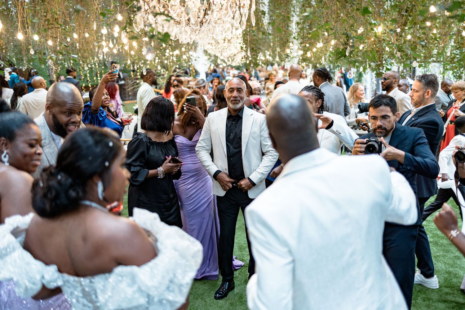 Wedding reception celebration with guests dancing outdoors under trees.