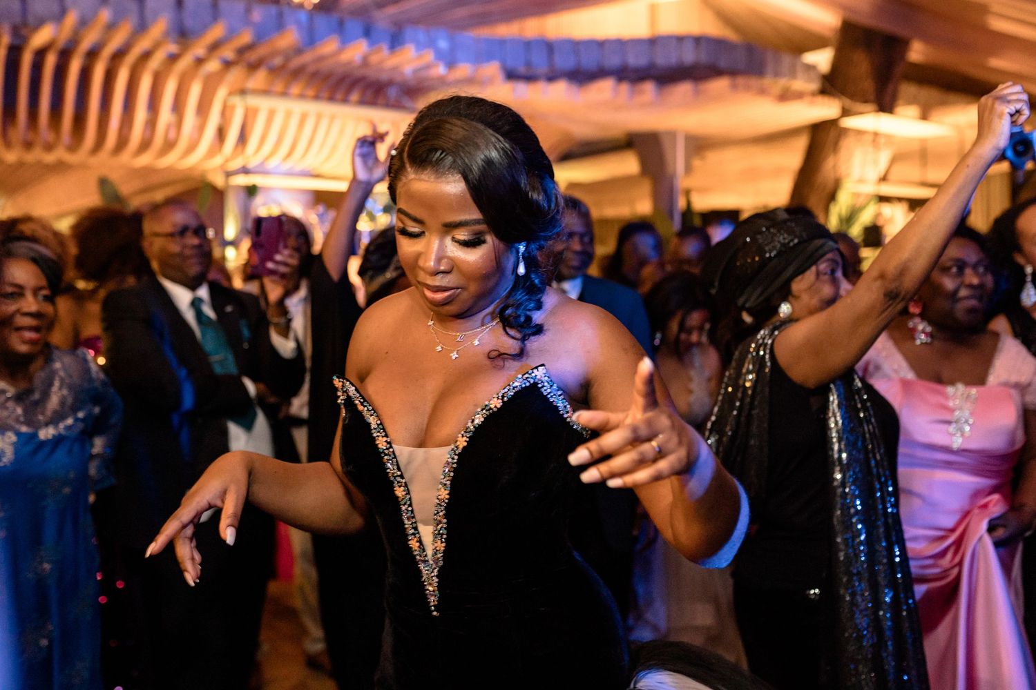 Wedding guests dancing and celebrating at a lively indoor reception with colorful lighting.