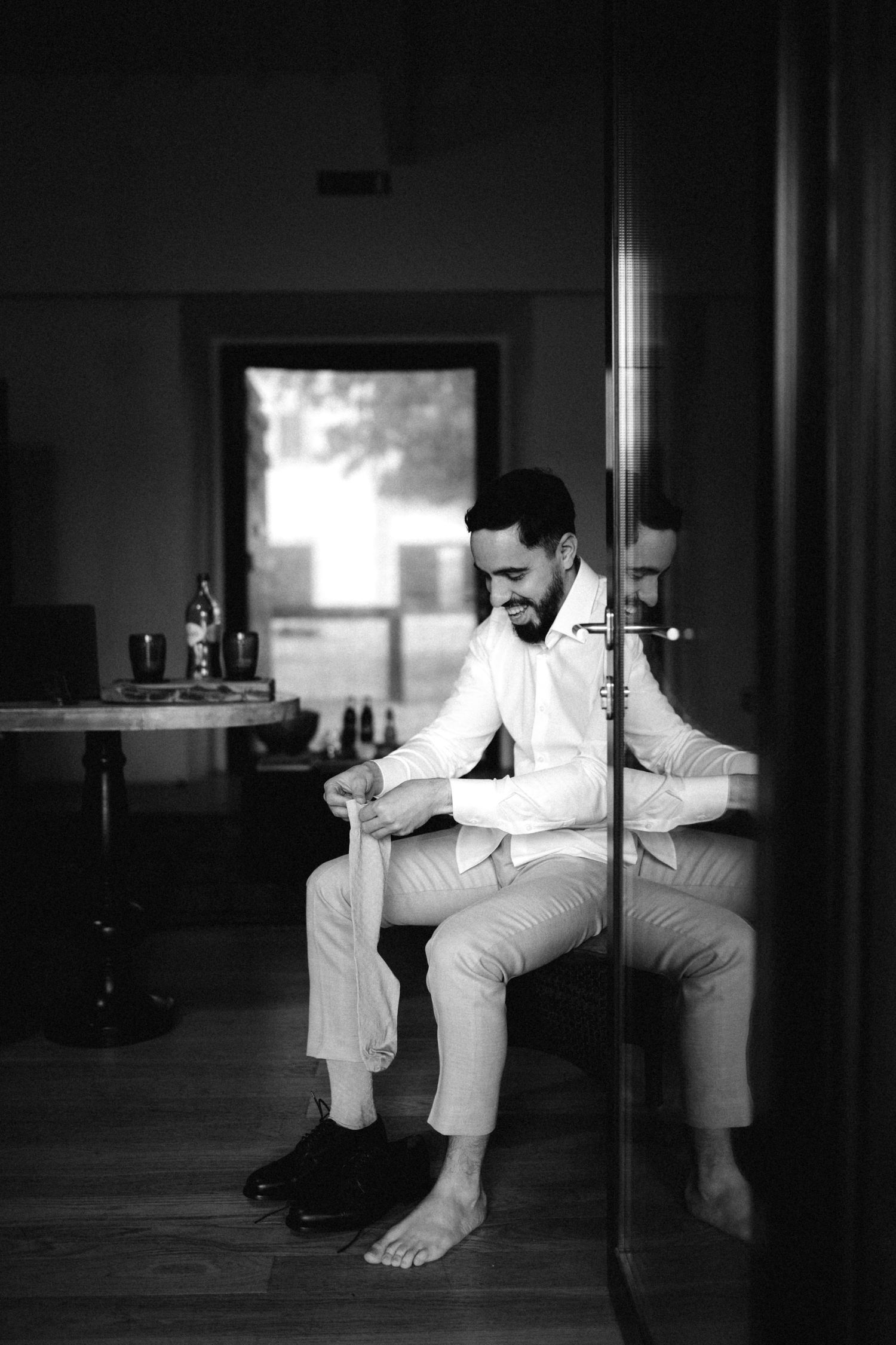 Black and white photo of someone in white attire sitting on a chair in a minimalist setting.