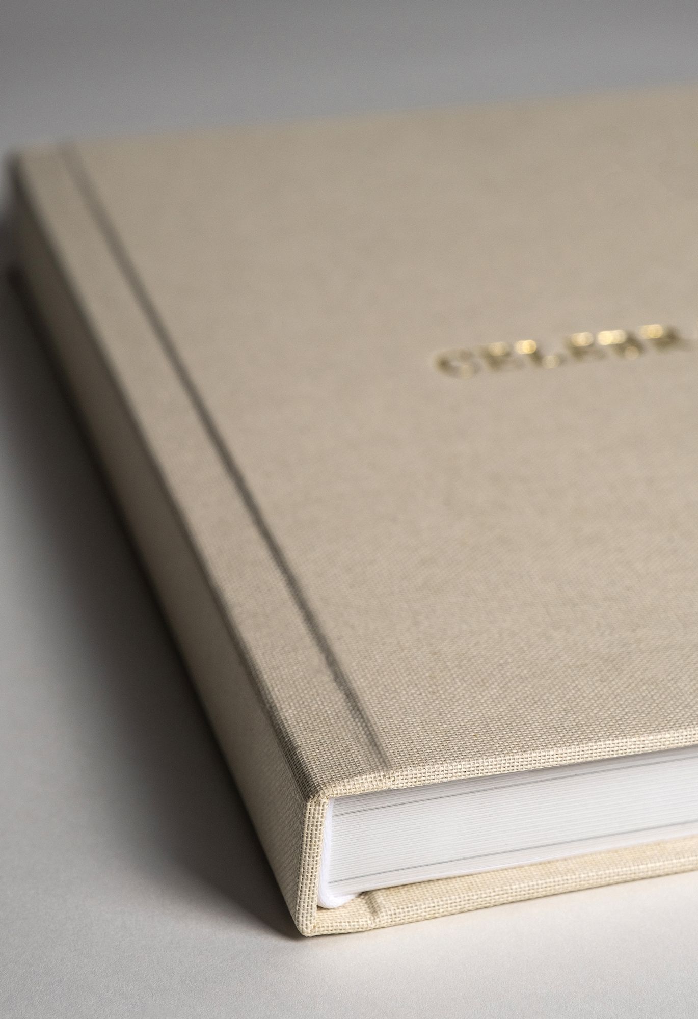 Close-up view of a minimalist beige linen notebook with gold lettering detail and white pages.