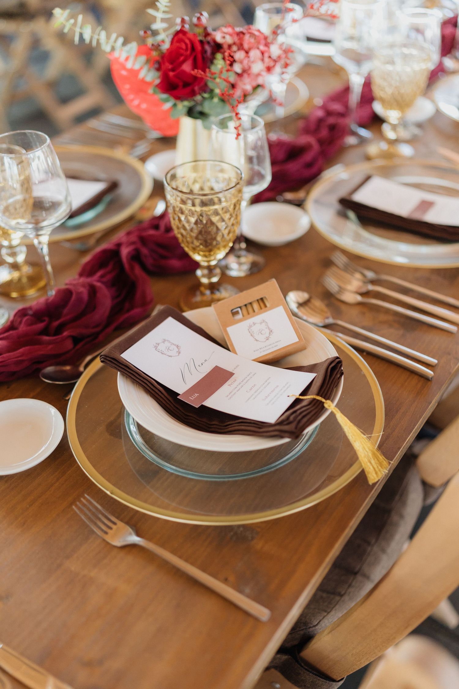 Rustic wooden table settings with gold chargers and burgundy accents for a wedding reception.