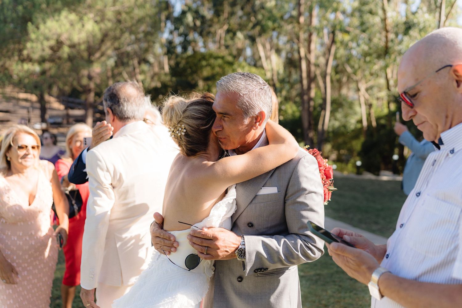 Wedding guests celebrating outdoors with joyful embraces in natural sunlight.