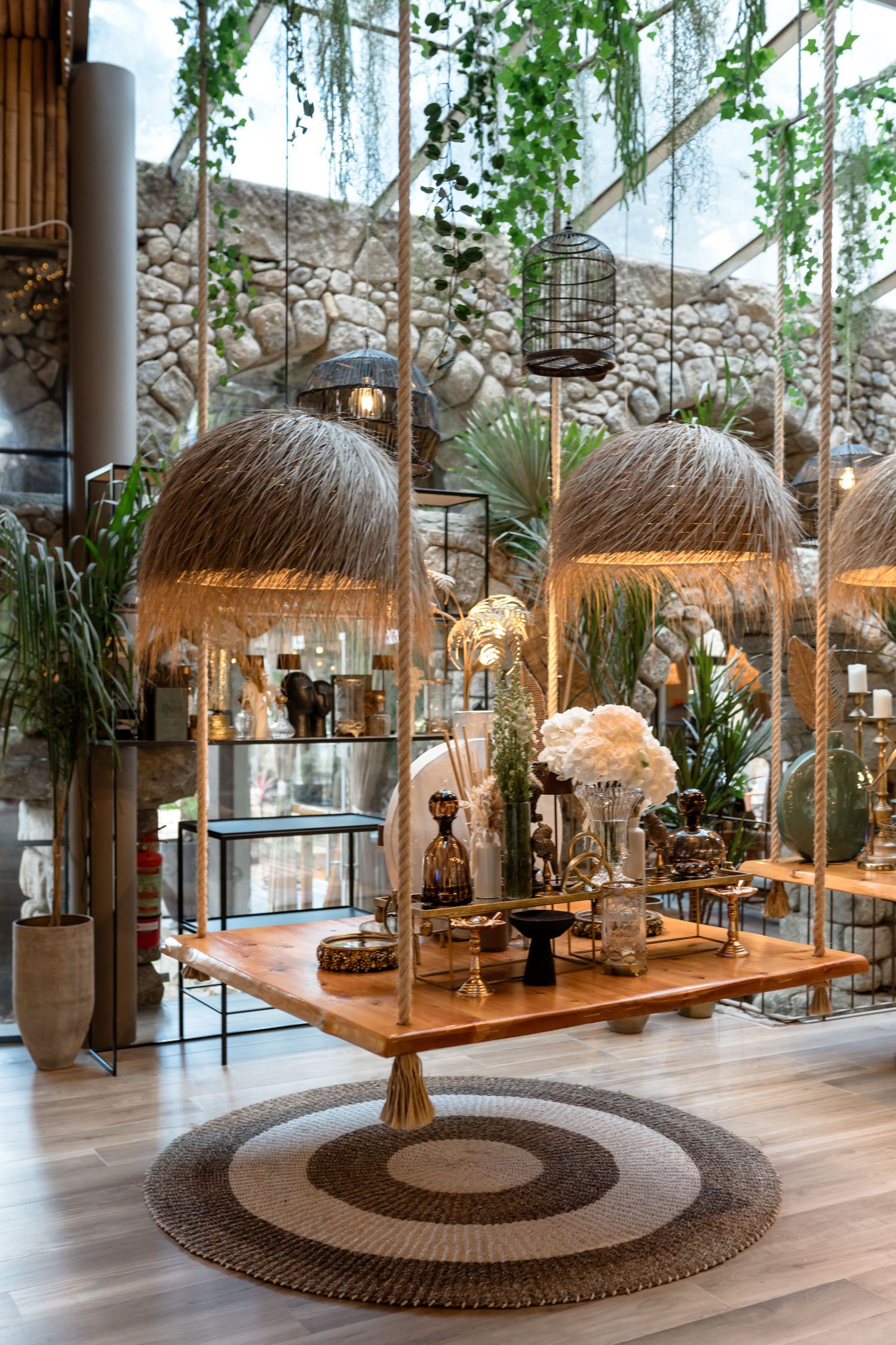 Tropical-inspired retail display with thatched roof fixtures and hanging plants against a stone wall.