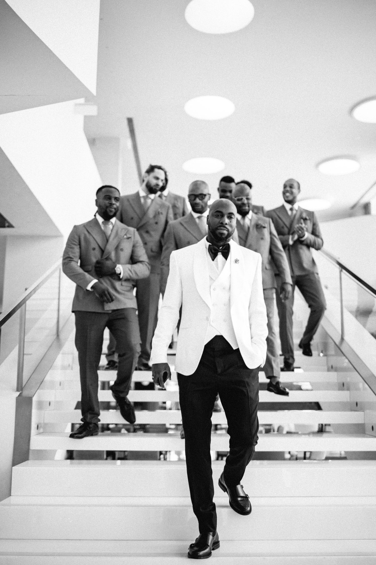 Groomsmen in white dinner jackets descending modern white stairs.