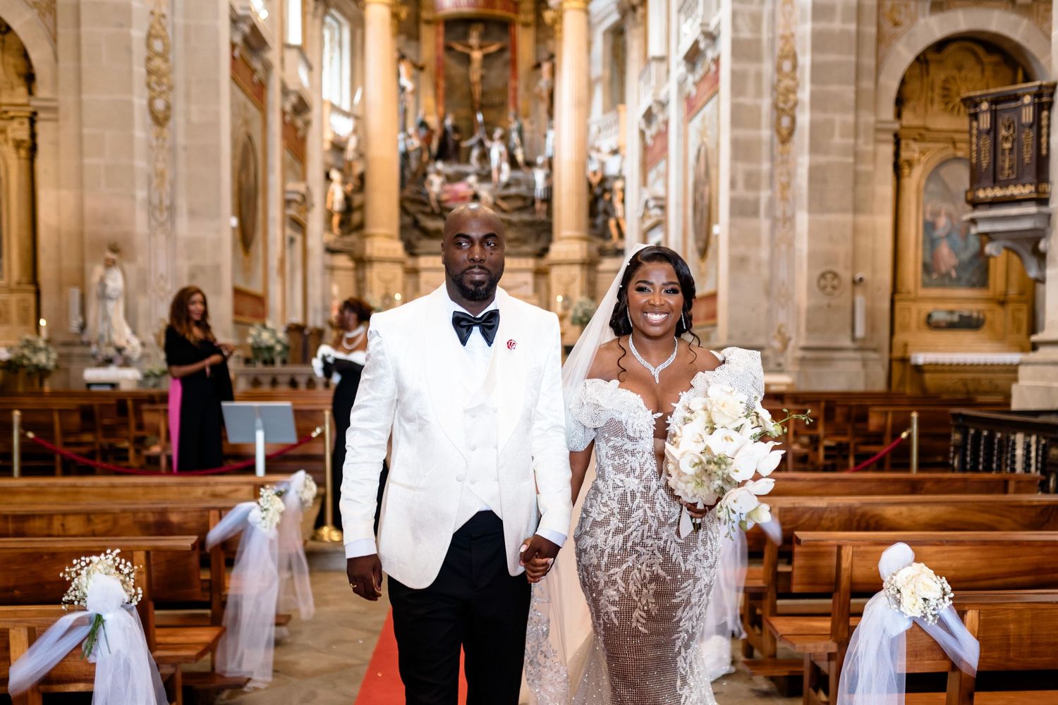 A newlywed couple walks down the aisle of a grand church after their ceremony.