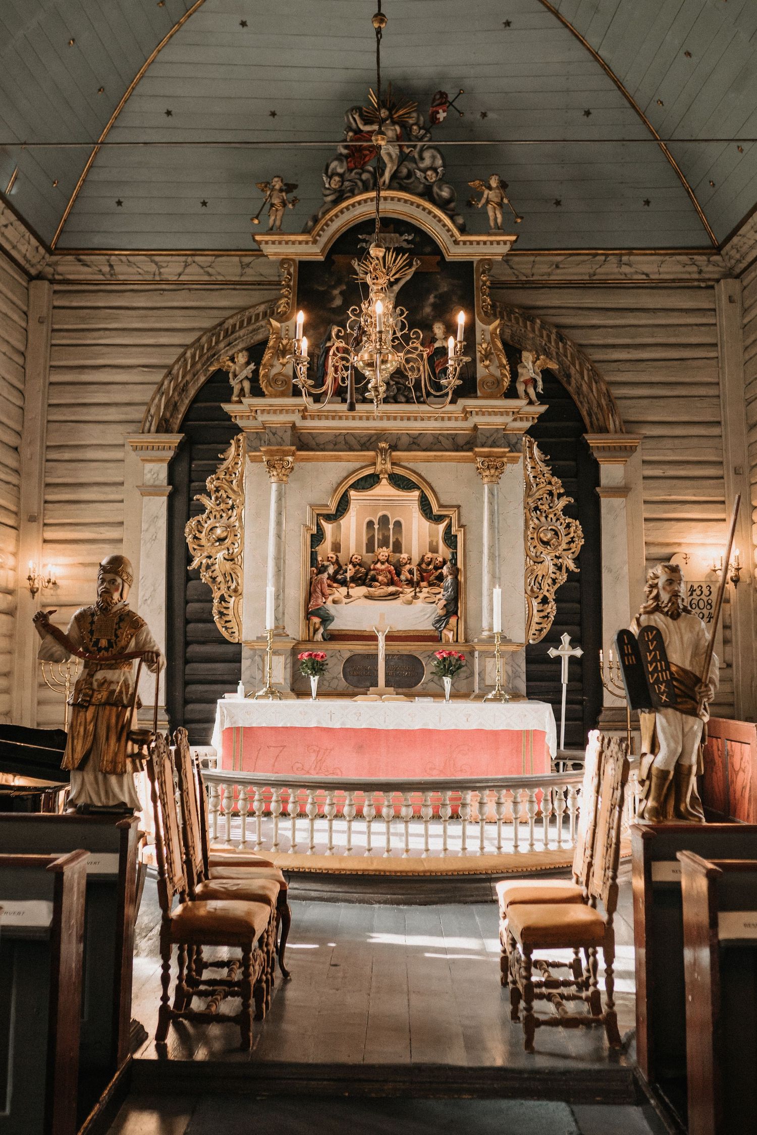 Interior of a traditional wooden church with ornate altar featuring religious sculptures and decorative elements.