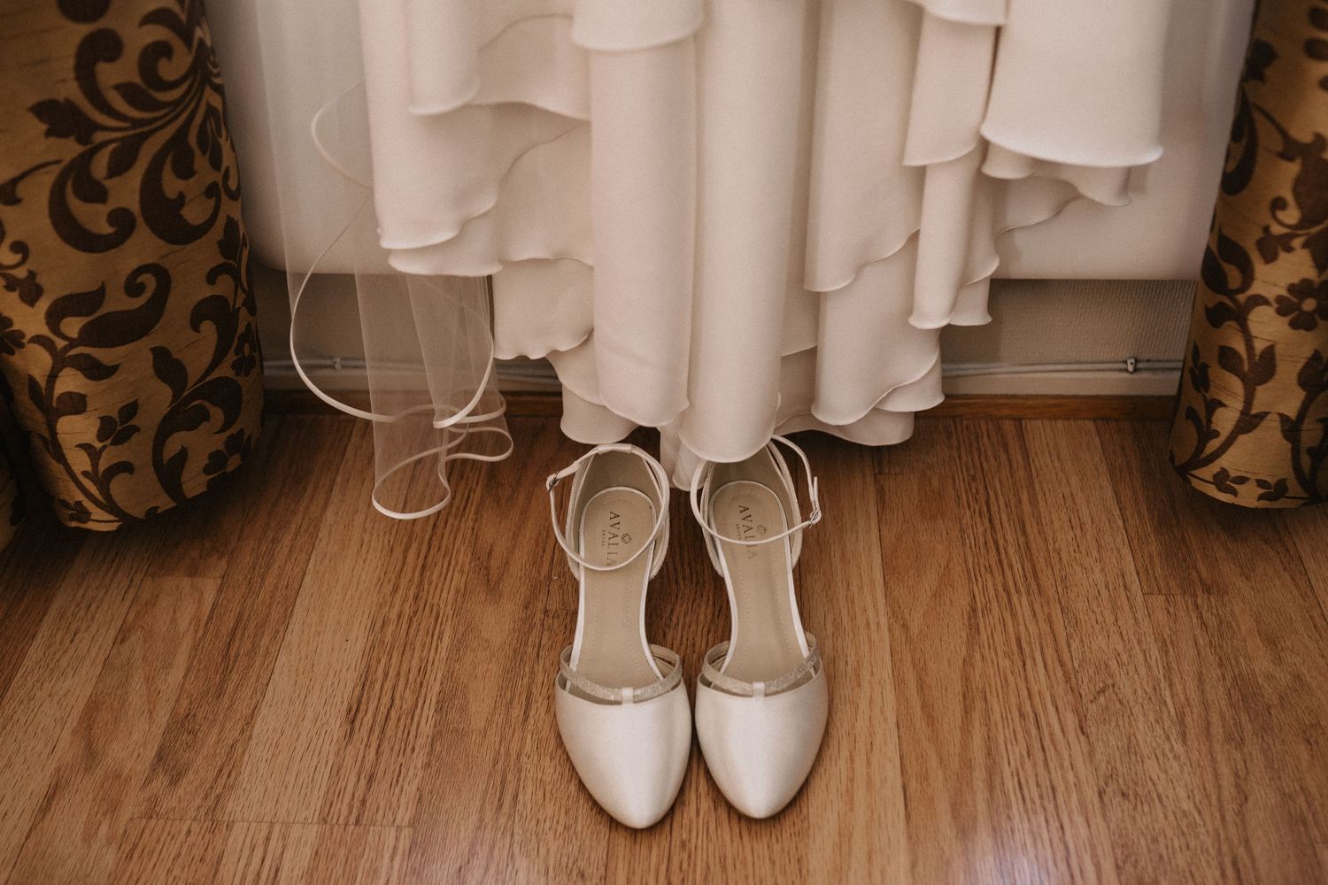 White bridal shoes on wooden floor against white curtains.
