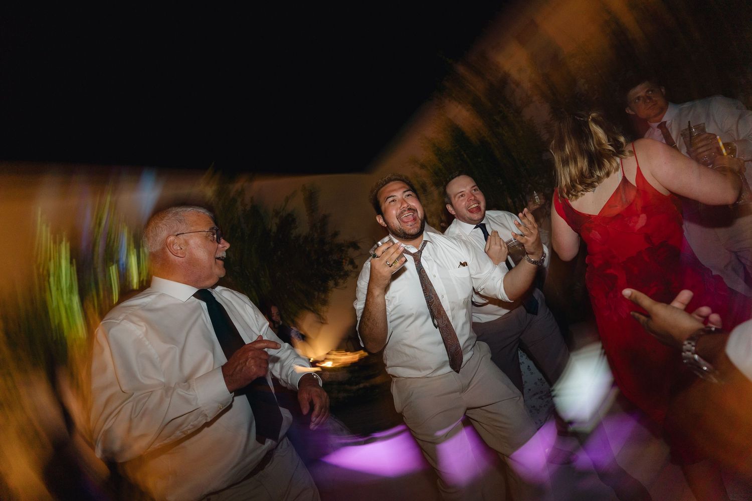 Crowded dance floor with people celebrating under purple and yellow lighting effects.