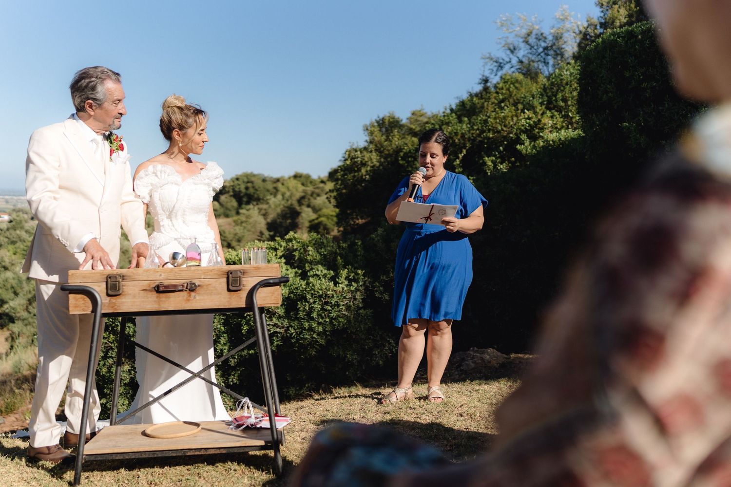 Guests relax on wooden benches during an outdoor wedding reception.