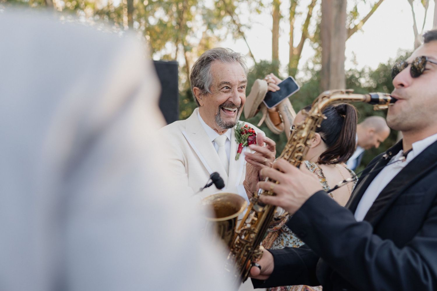 Outdoor wedding reception with guests dancing under trees.