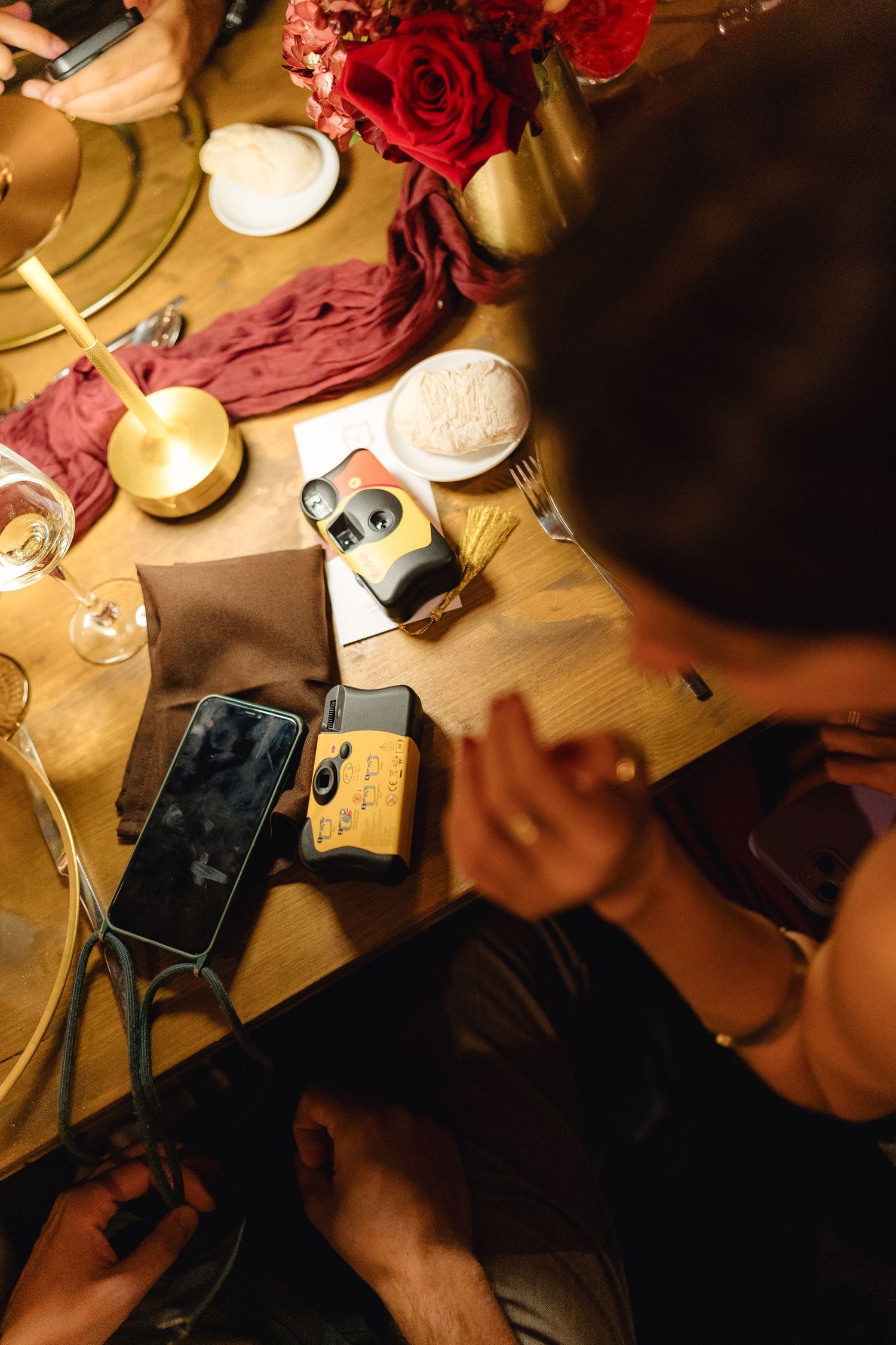 Close-up of table settings with red roses, wine glasses, and mobile phones in warm candlelight.