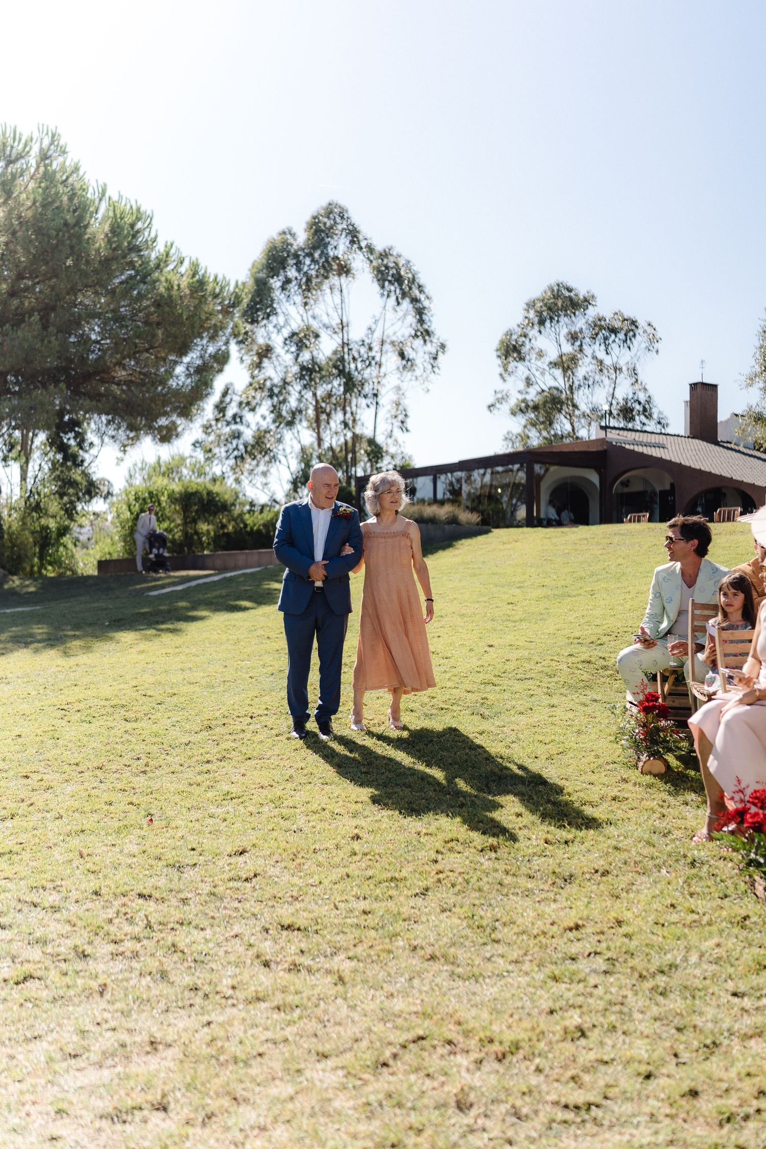 Wedding guests walk across a grassy hill during an outdoor celebration.
